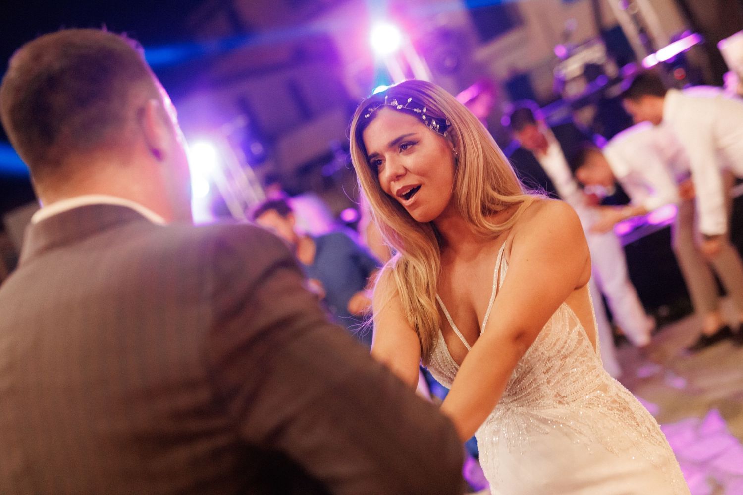 Couples slow dance together on a purple-lit dance floor during a formal wedding reception celebration.