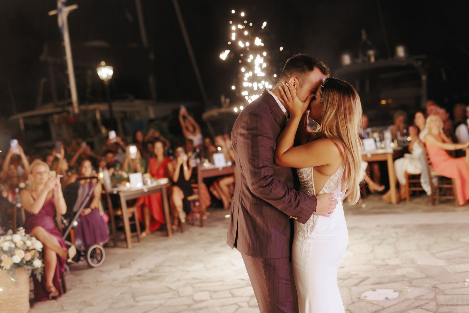 Couples dance together on an outdoor dance floor at a romantic evening reception with glowing string lights overhead.