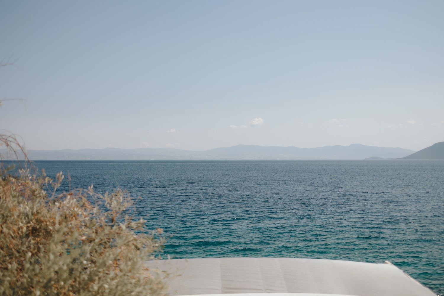 Panoramic view of a tranquil blue ocean with distant mountains under a clear sky along a rocky coastline.