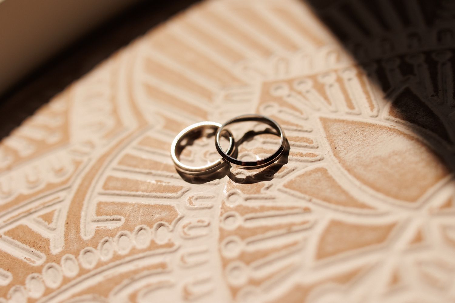 Two wedding rings resting on a decorative beige patterned surface in a sepia-toned photograph.
