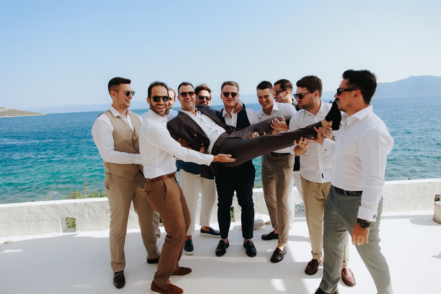A cheerful group in white shirts and khakis line up at a beach doing coordinated dance moves together at sunset.