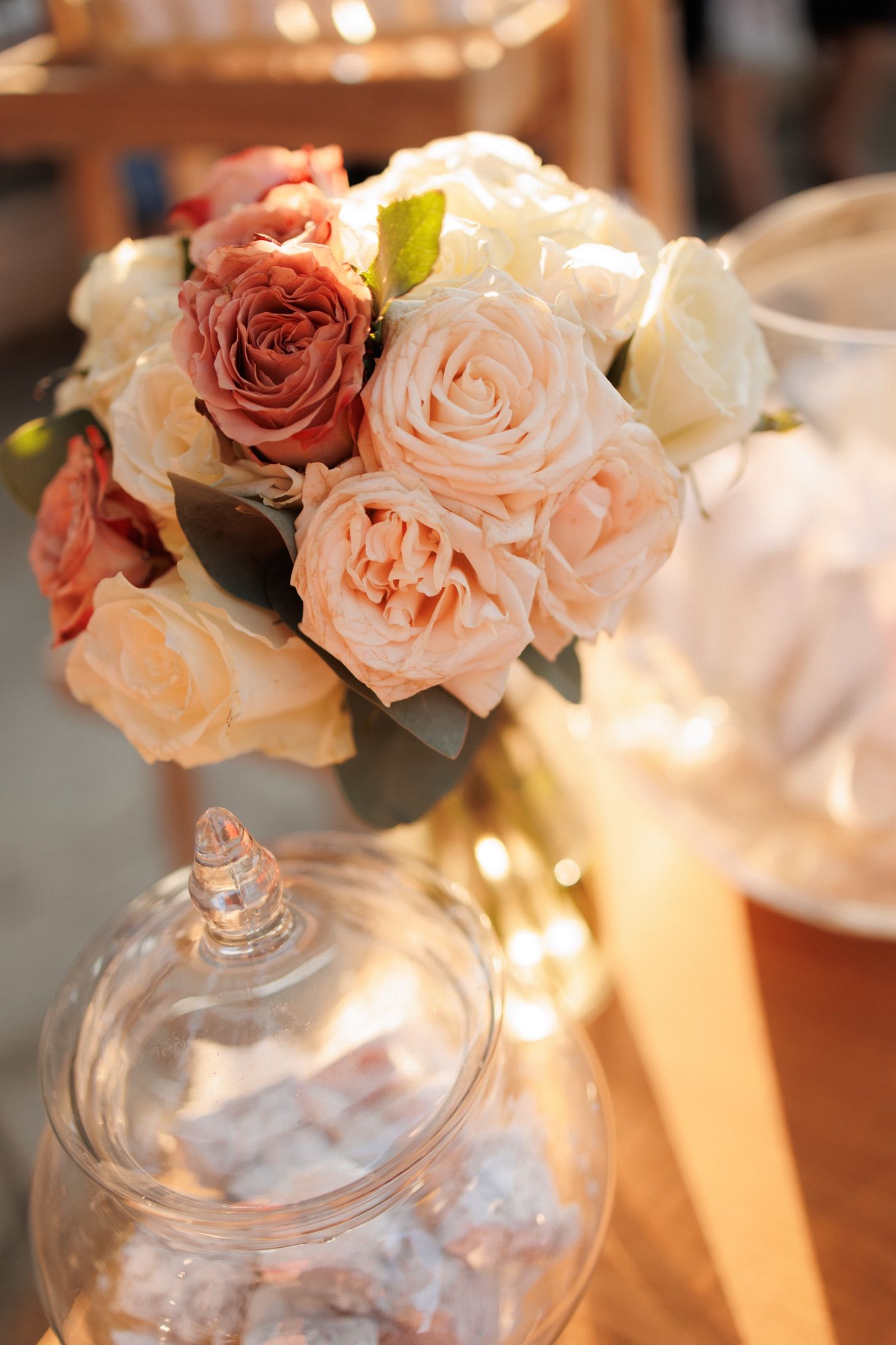 Crystal glass apothecary jar decorated with delicate pink and ivory roses in soft romantic lighting.
