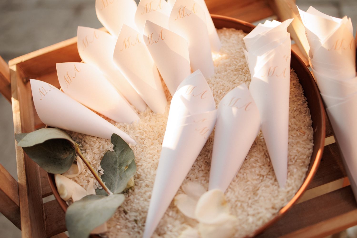 White paper piping bags filled with frosting sit nestled in sugar inside a wooden container.