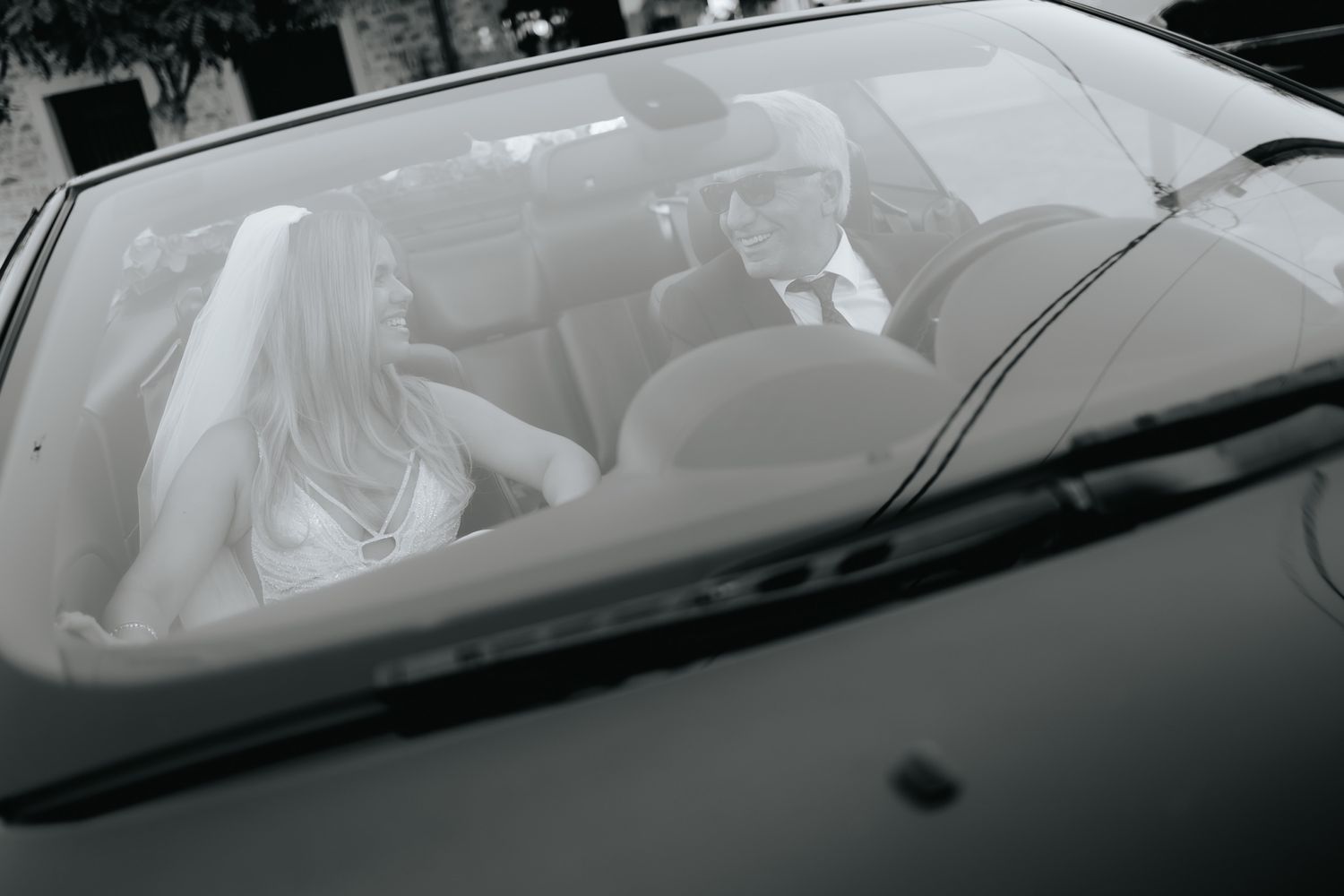 View through a car windshield showing people sitting in the front seats, captured in black and white photography.