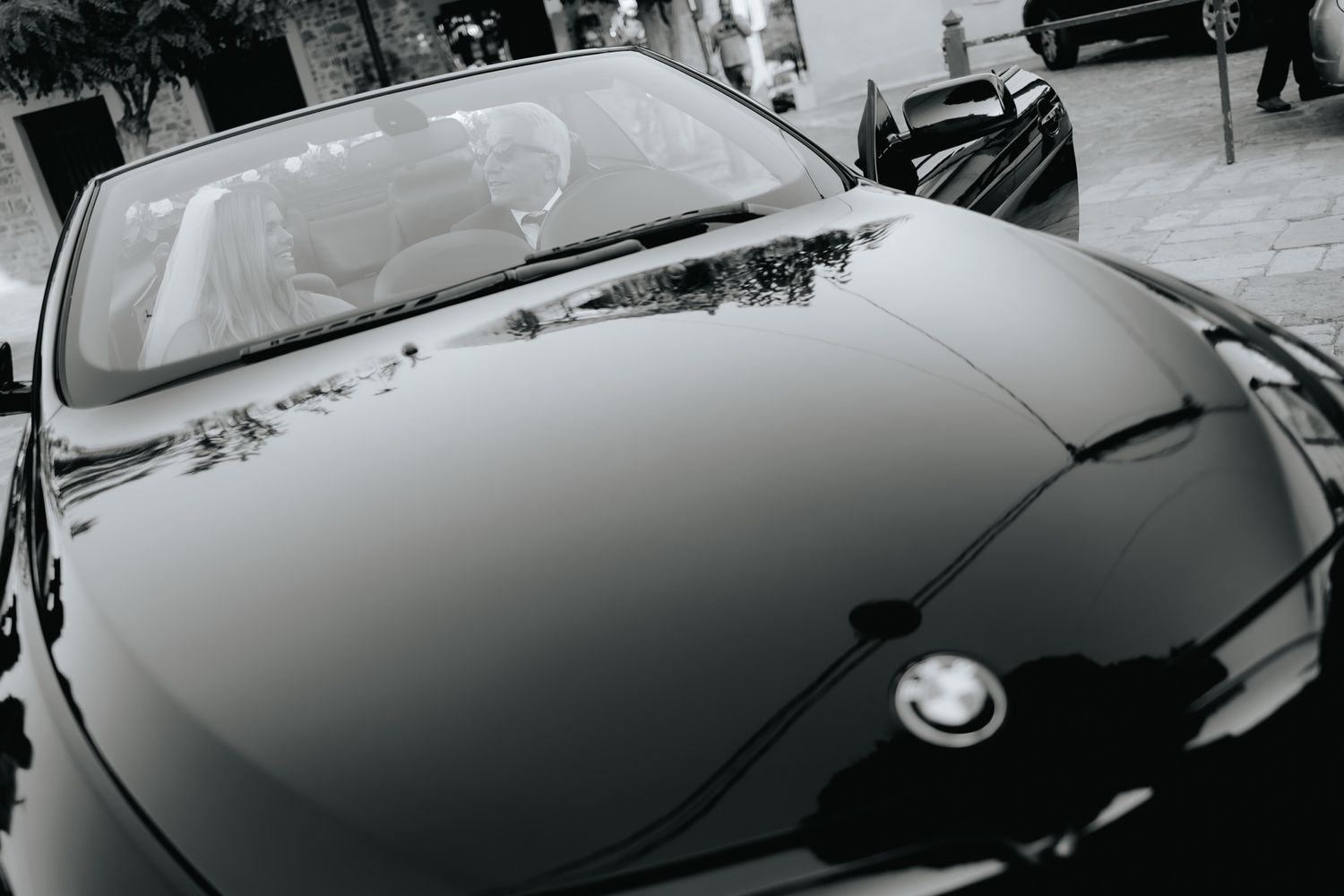 Black and white close-up photo showing the hood and windshield of a sleek BMW luxury car.