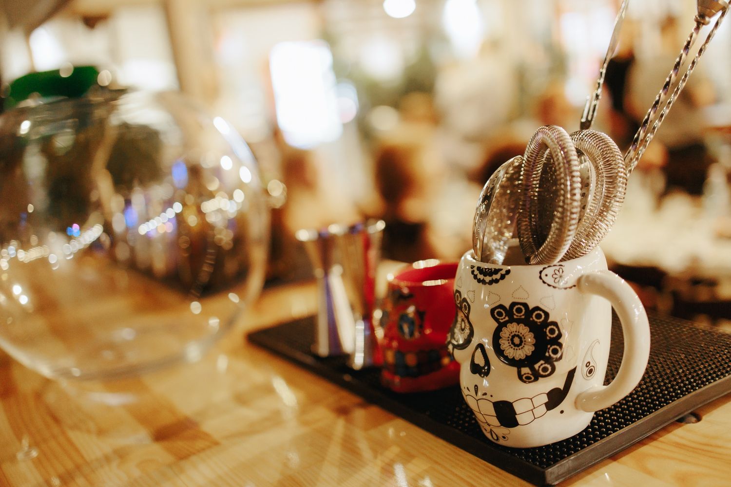 Multiple mugs with decorative designs and coffee cups sit on a blurred wooden surface in warm lighting.