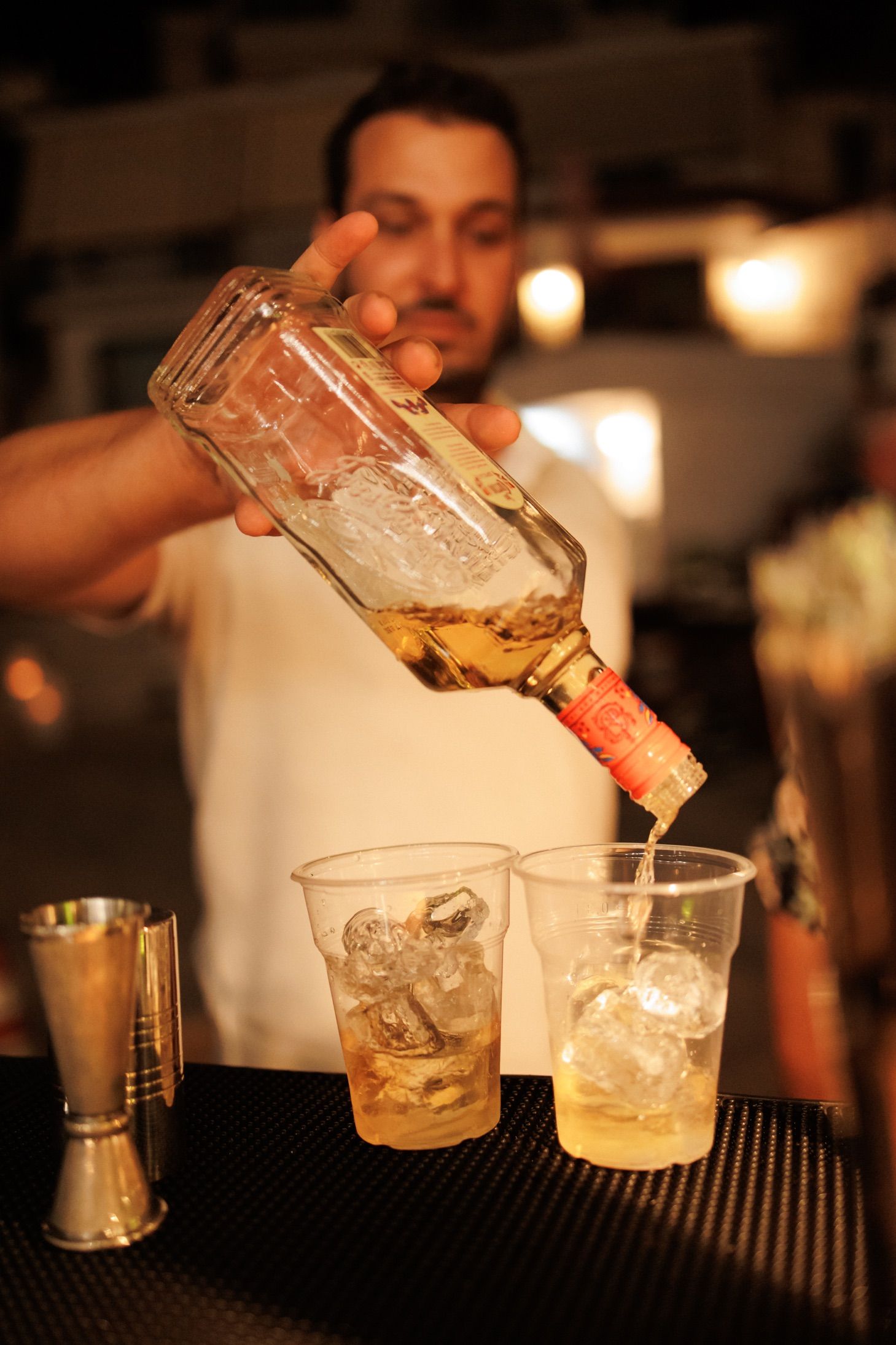 Bartender pouring multiple craft cocktails with precise measurements at a dimly lit bar counter.