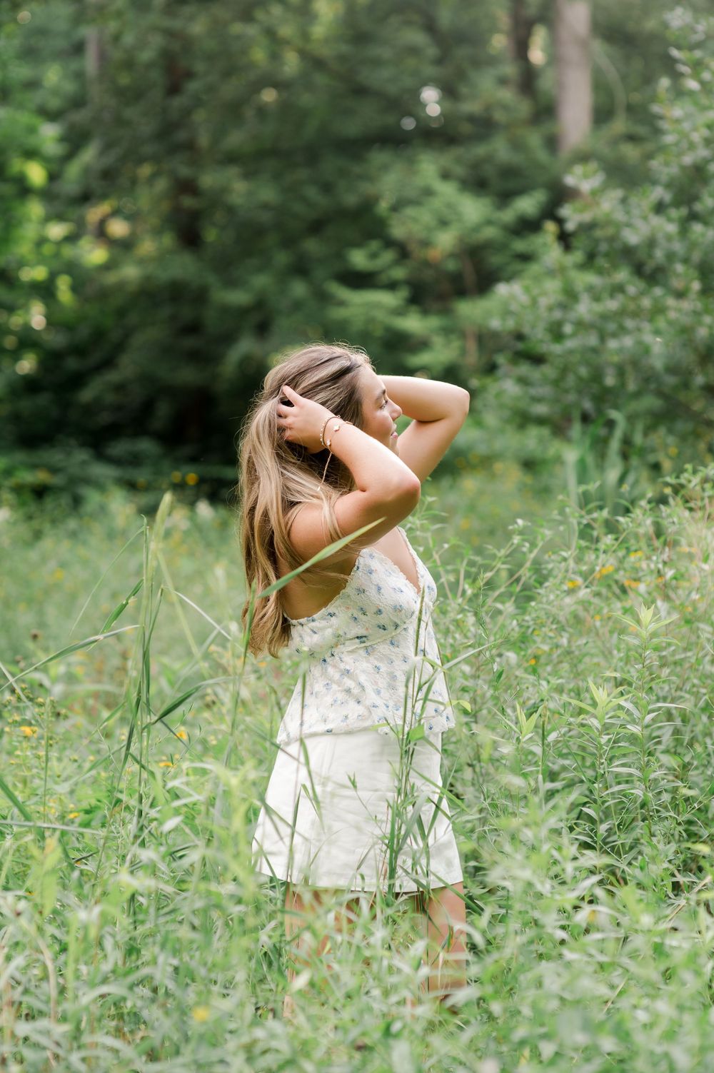A figure in a white summer dress stands amid tall grass and greenery in a dreamy outdoor setting.