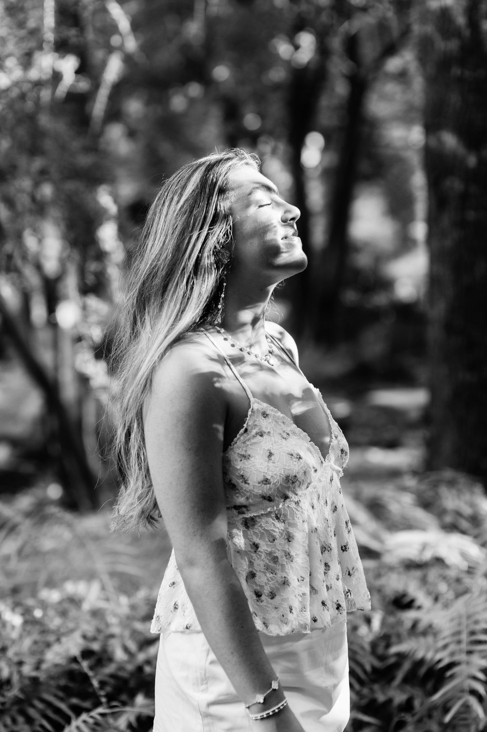 A series of black and white photos show a person in a floral dress laughing outdoors surrounded by ferns in nature.