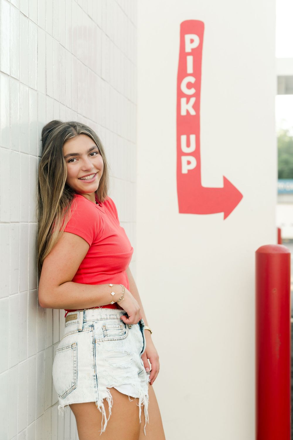 A red t-shirt and denim cutoff shorts ensemble is shown next to a red pickup arrow sign on a white wall.