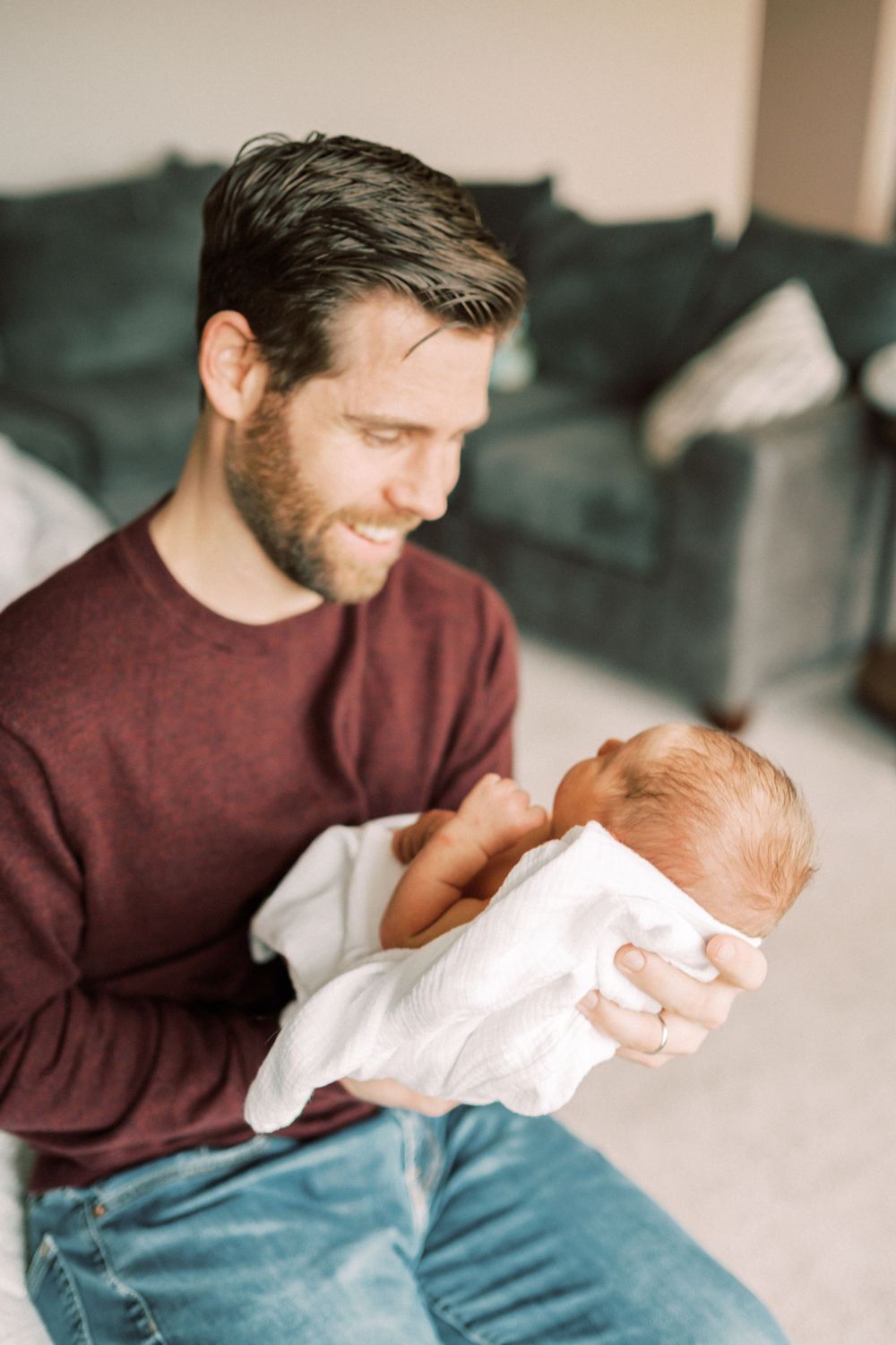A tender moment captured as a person in a burgundy sweater lovingly holds a swaddled newborn baby.