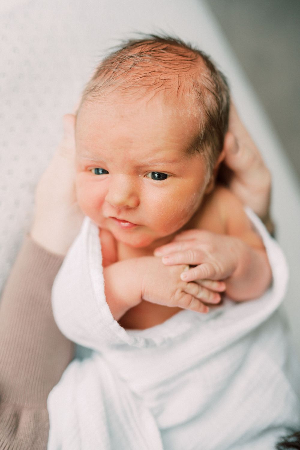 Close up portrait of an alert newborn baby wrapped in white swaddling cloth.