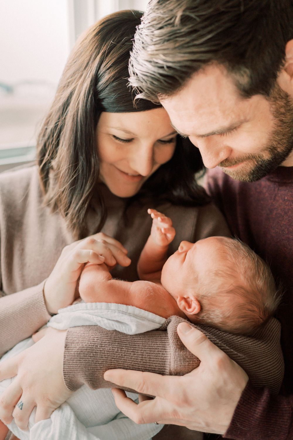 Intimate close-up of parents gazing lovingly at their newborn baby wrapped in soft clothing.