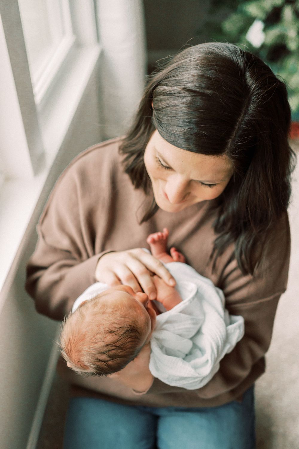 Tender moment as caregiver holds sleeping newborn wrapped in white blanket near window.