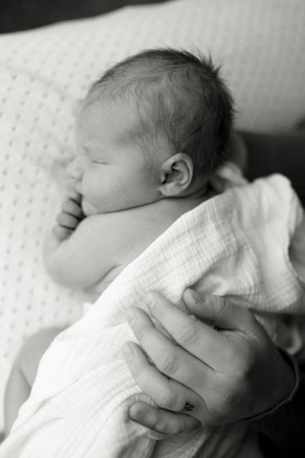 Black and white portrait of sleeping newborn wrapped in soft white blanket.