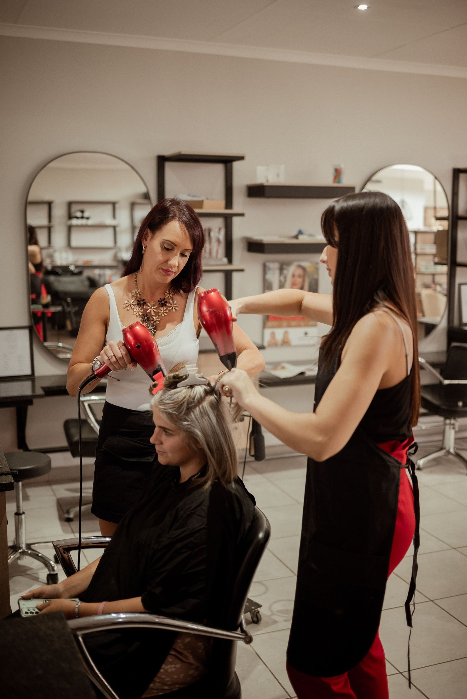 Two hairstylists work together on client's hair in modern salon with arched mirrors.