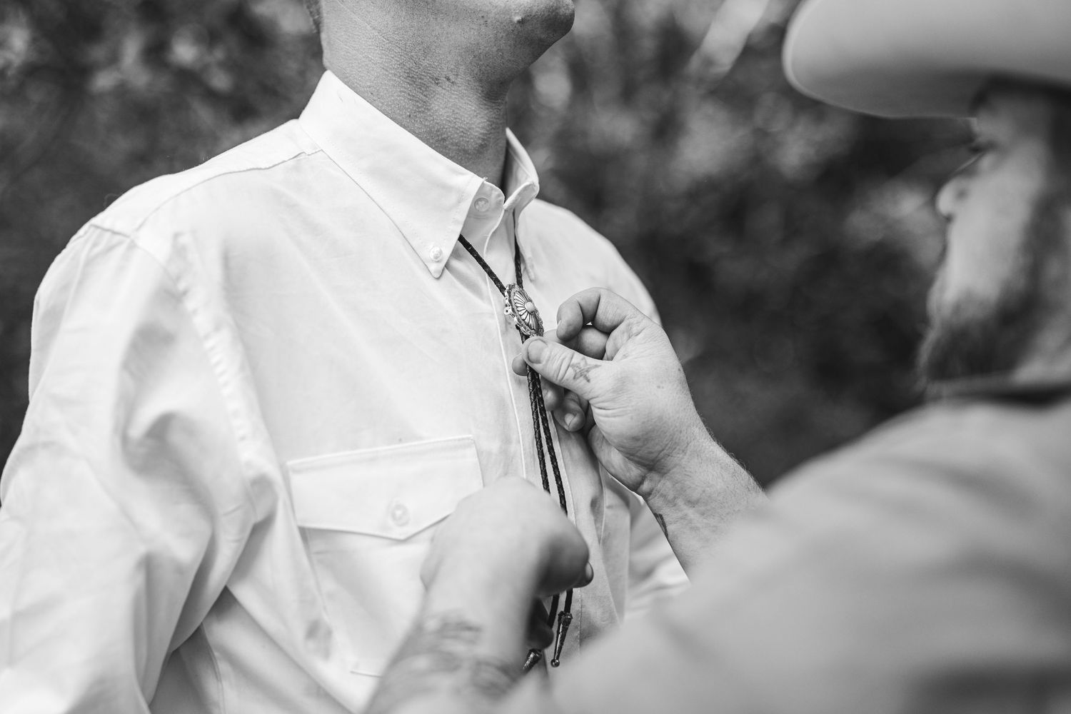 Black and white photo of someone helping pin a boutonniere flower onto the lapel of a white dress shirt.