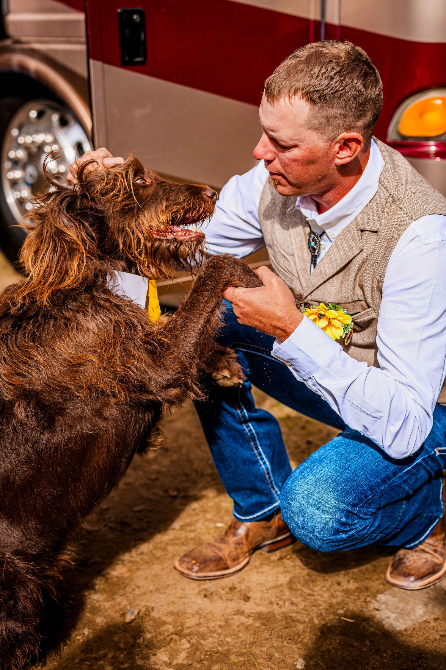 A person in casual attire pets a large brown shaggy dog in a rustic setting.
