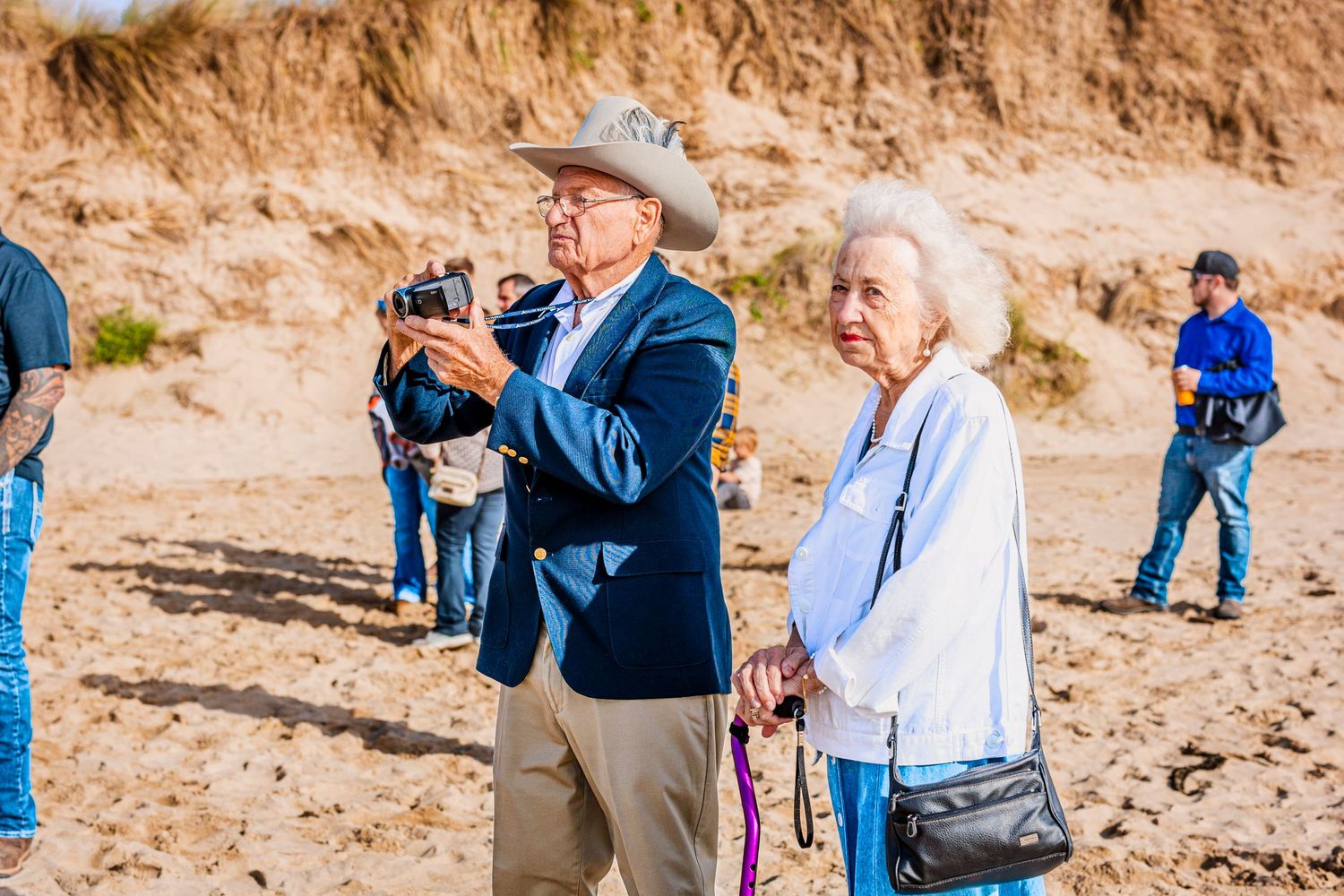 Elderly guests explore a beach area with cameras during a special outdoor gathering.
