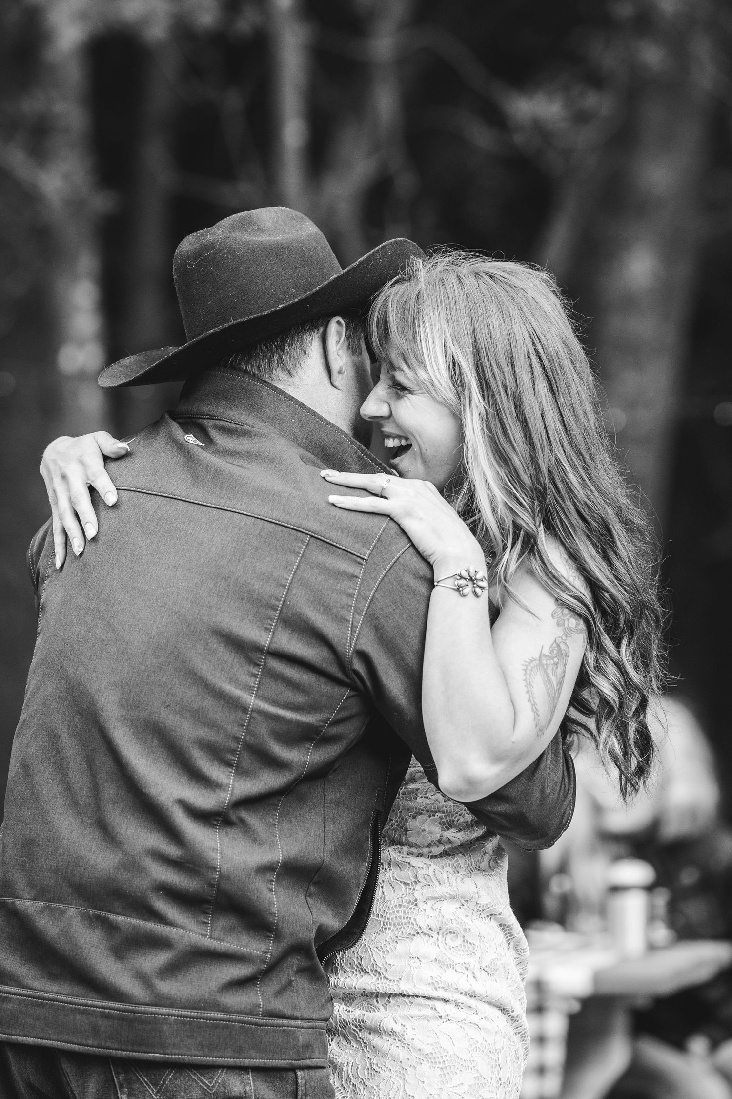 Black and white romantic portrait of a couple embracing and smiling during what appears to be an outdoor celebration.