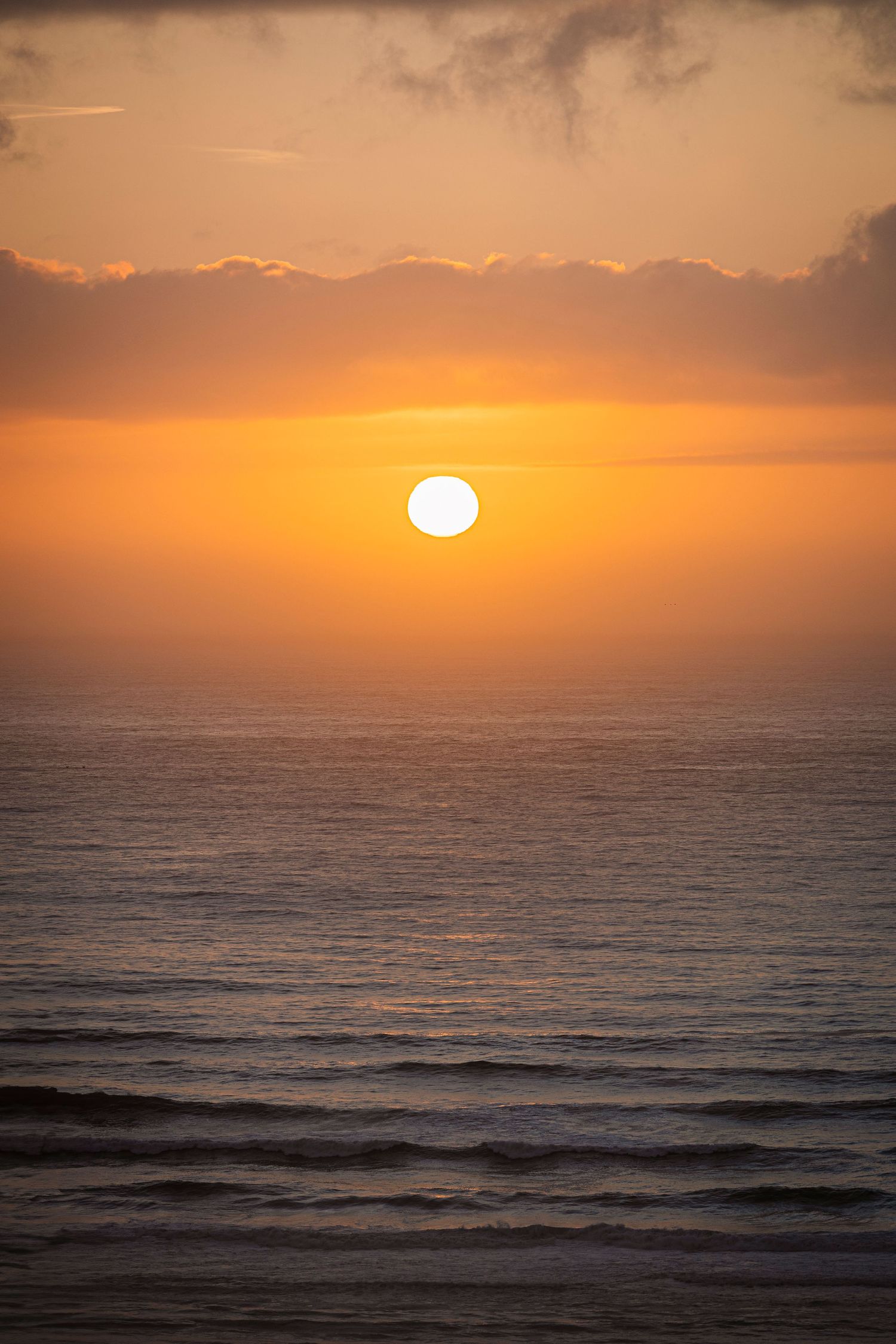 Vivid orange sunset over calm ocean waves with perfect round sun on horizon.