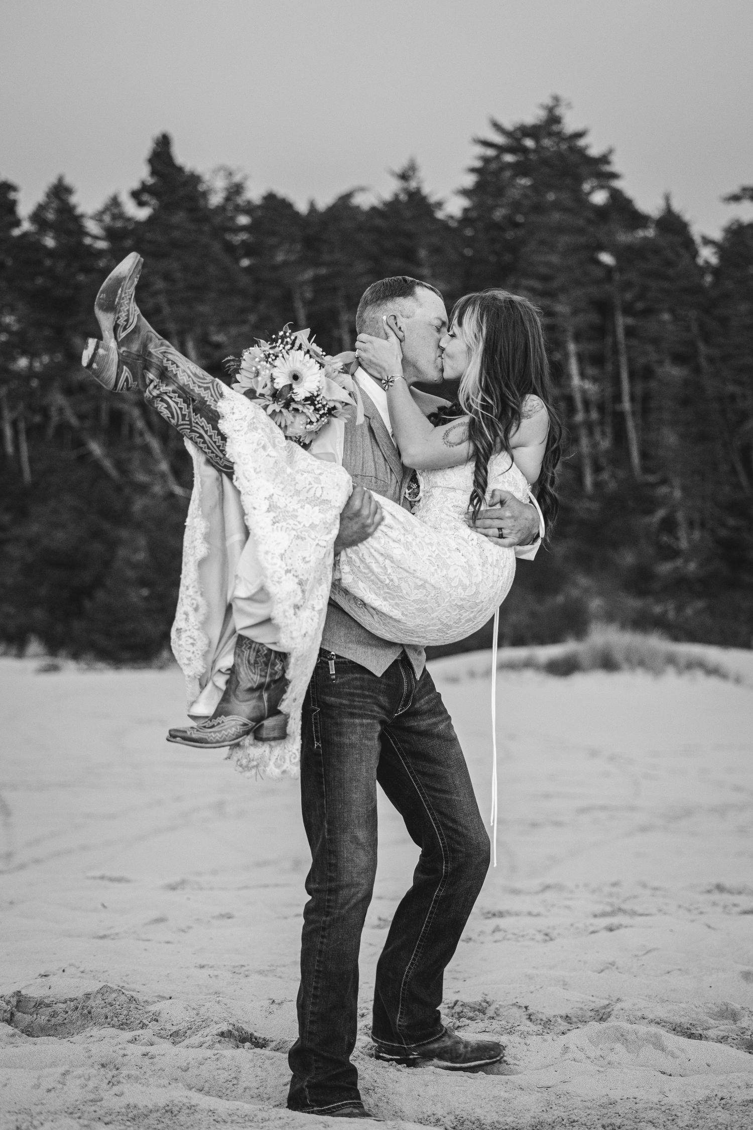 Black and white romantic beach portrait with evergreen forest backdrop.