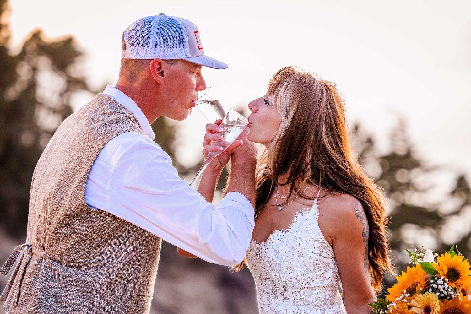 A candid moment between newlyweds sharing champagne at sunset during their rustic outdoor wedding.