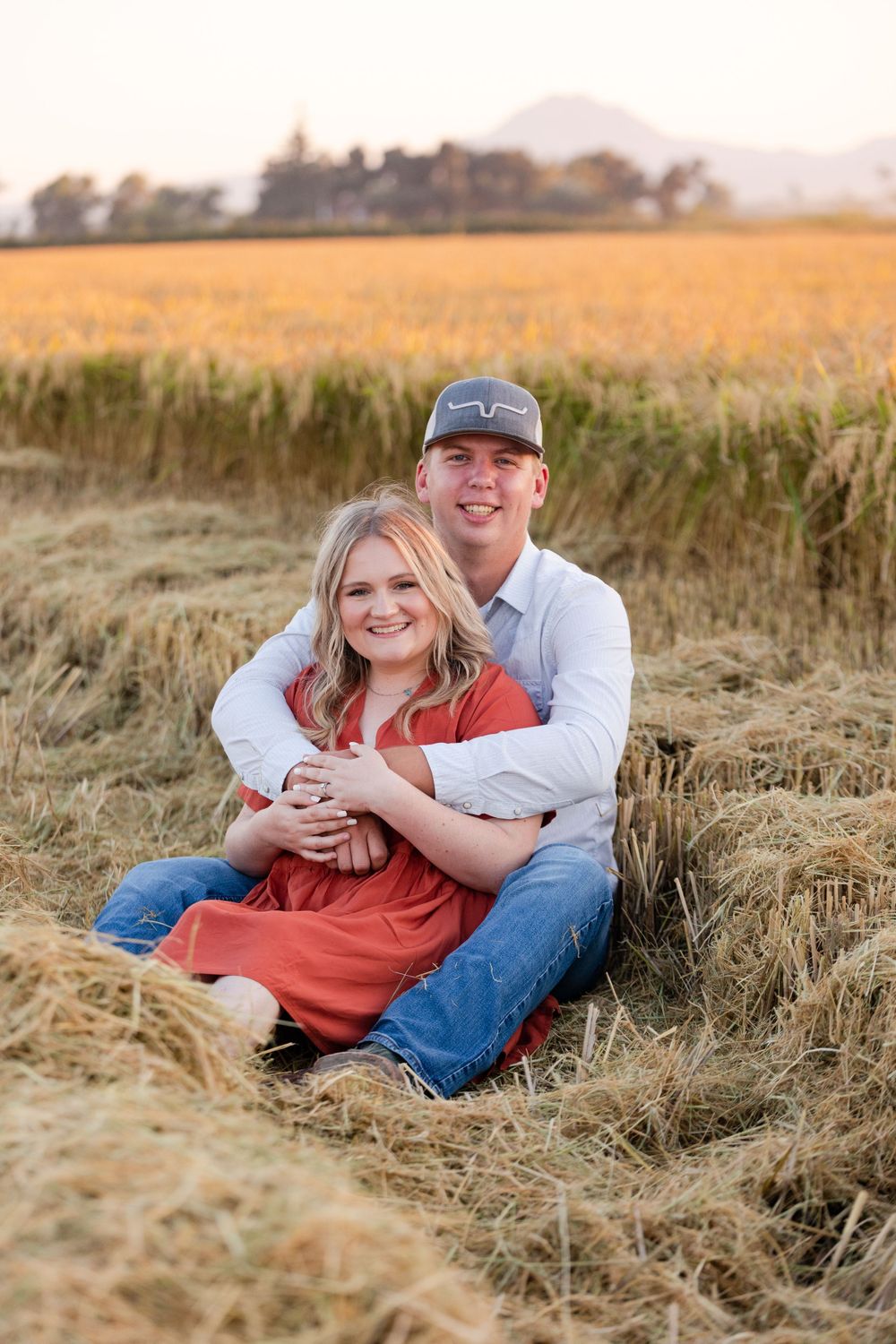 Couple sitting together in golden wheat field during sunset sharing an intimate moment.