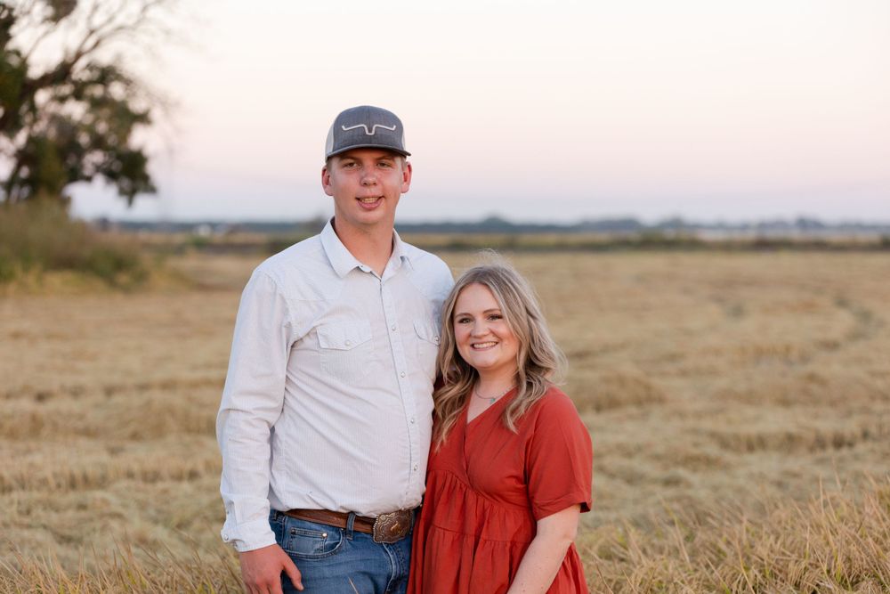 Couple stands together in an open field at sunset wearing white and rust colored outfits.