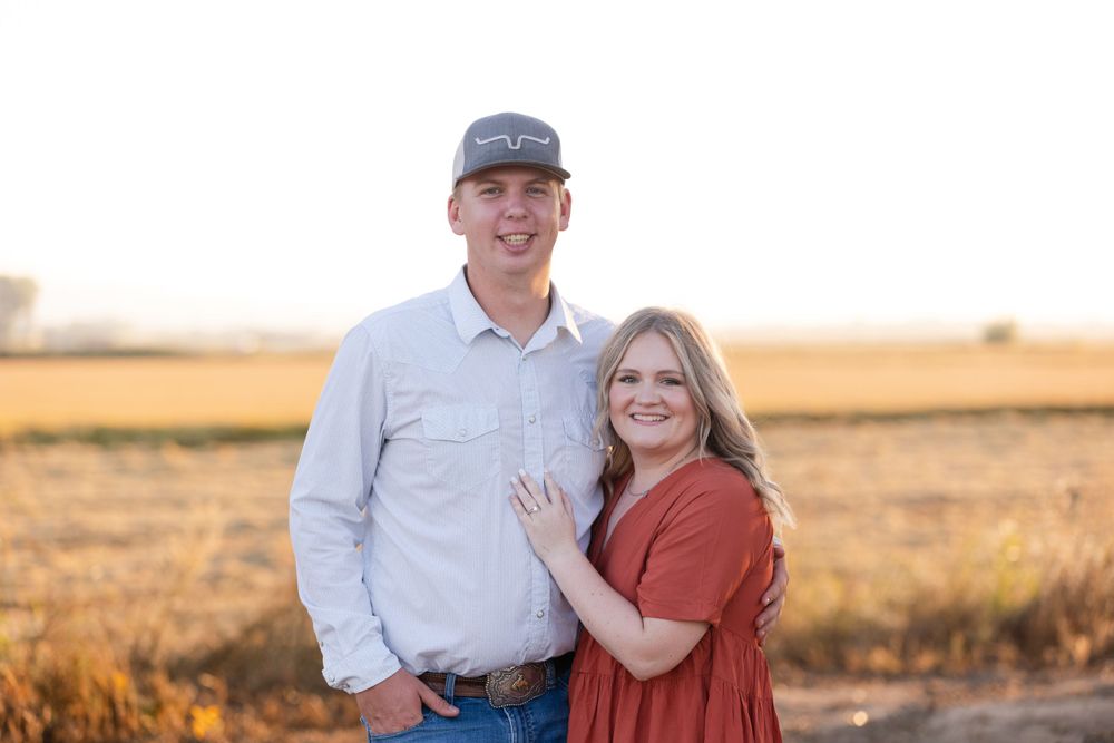 A couple poses together in a golden field at sunset with warm lighting and natural outdoor scenery.