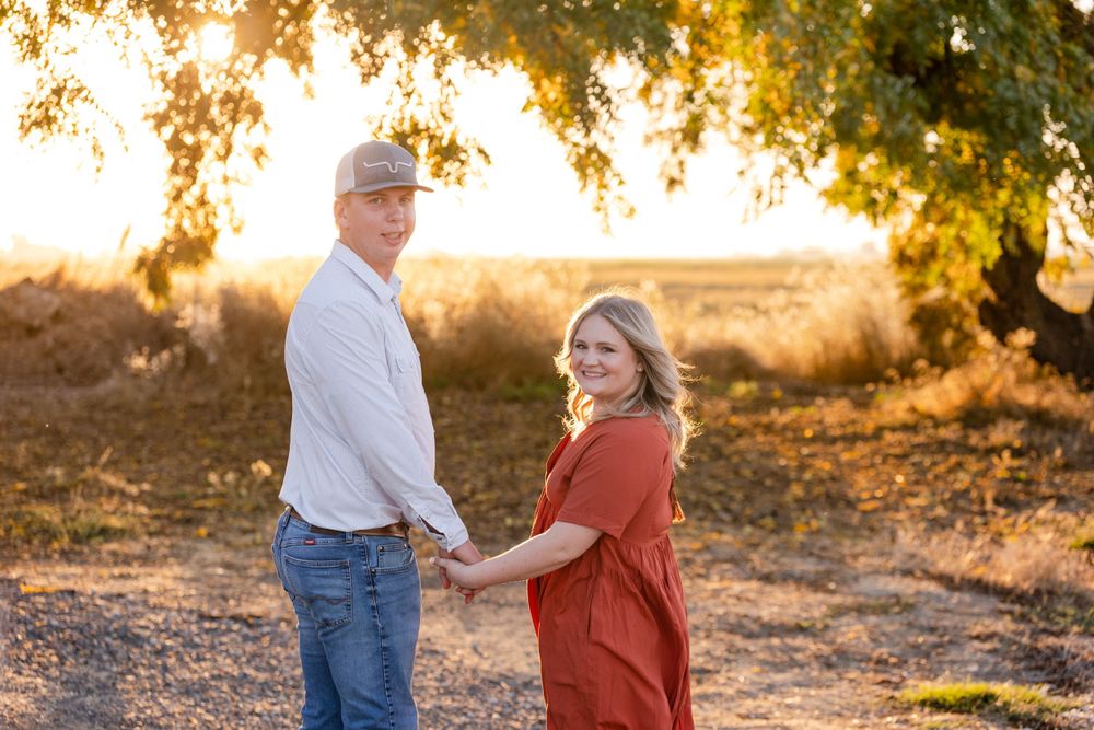 A couple shares a tender moment at sunset in a golden field with tree branches overhead.