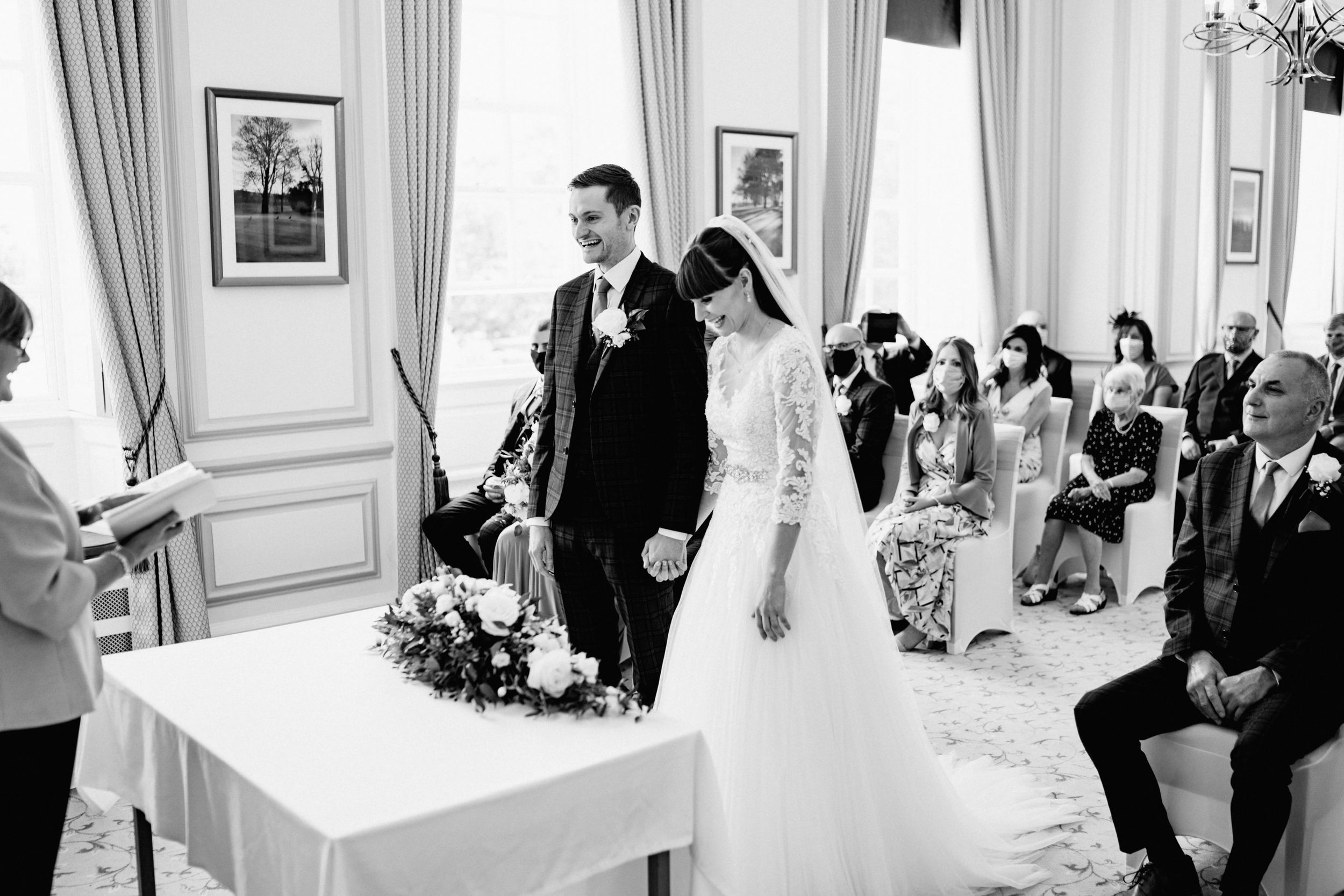 Wedding ceremony in elegant room with chandelier and white decor.