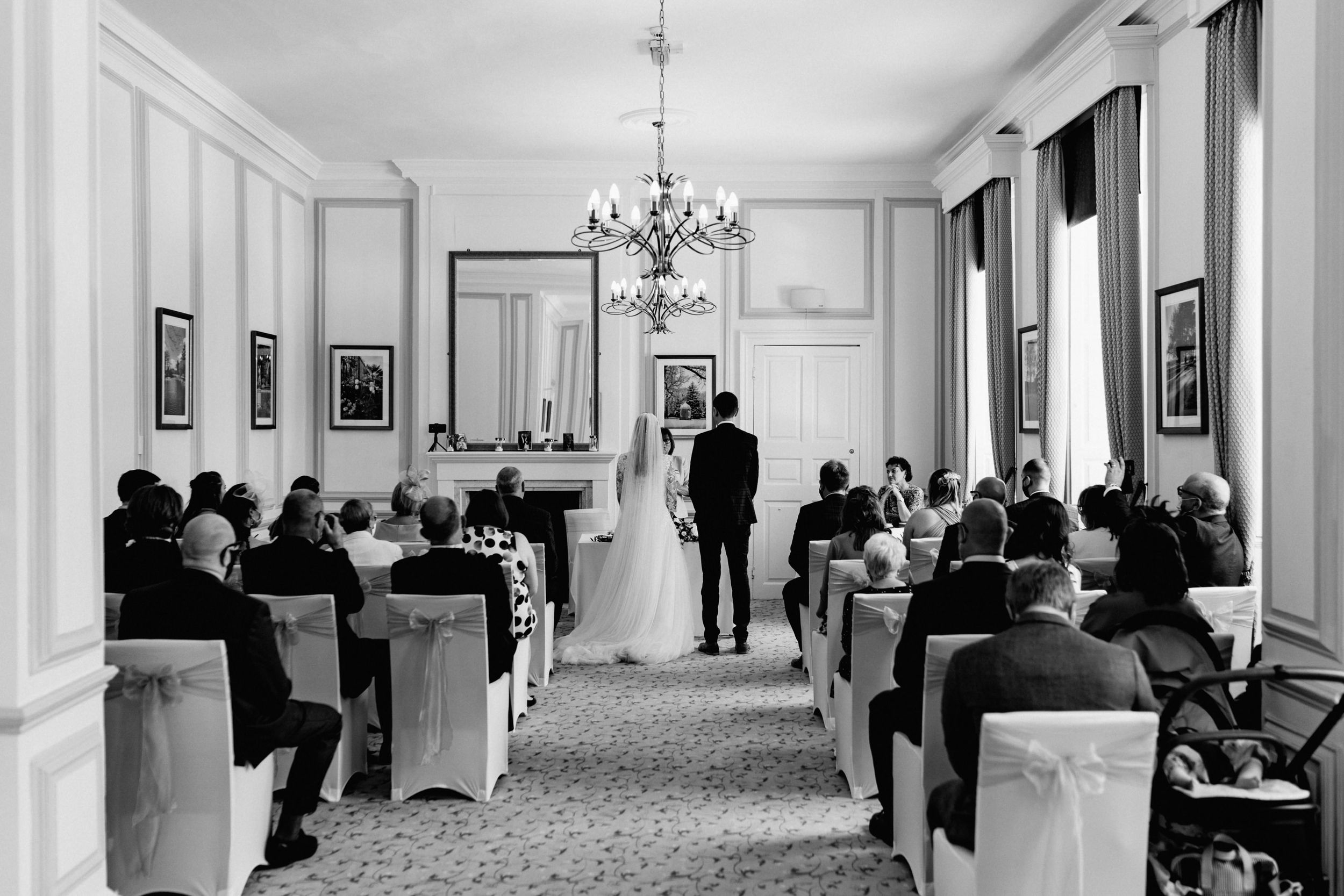 Black and white photo of intimate wedding ceremony in classic venue with chandelier, Harrowden Hall Northamptonshire.