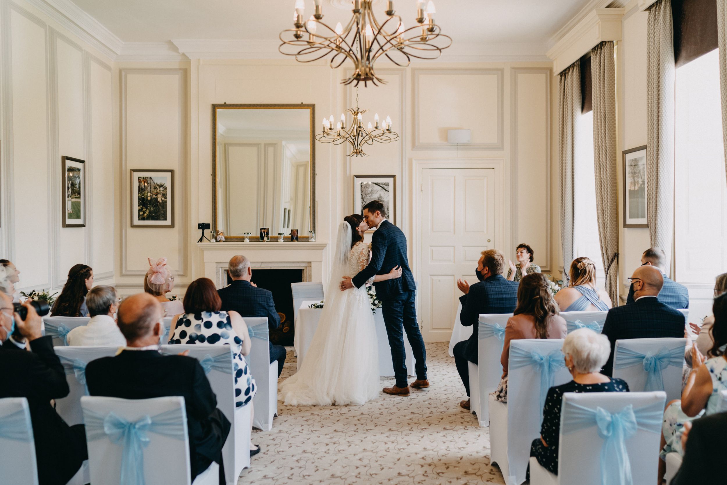 Elegant wedding ceremony at Harrowden Hall in bright room with blue chair decorations and chandelier.