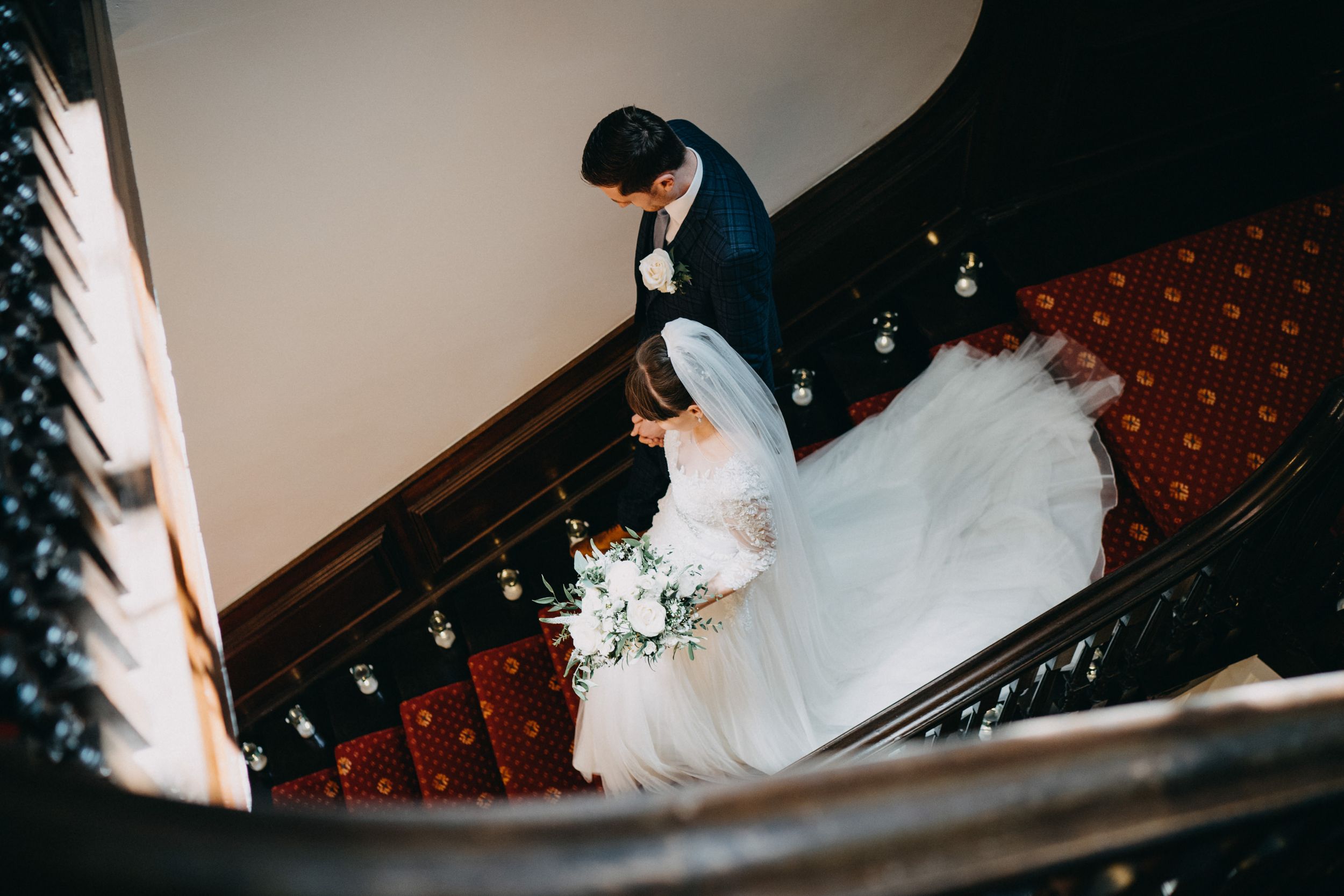 A couple descends an ornate staircase with flowing white dress trailing behind.