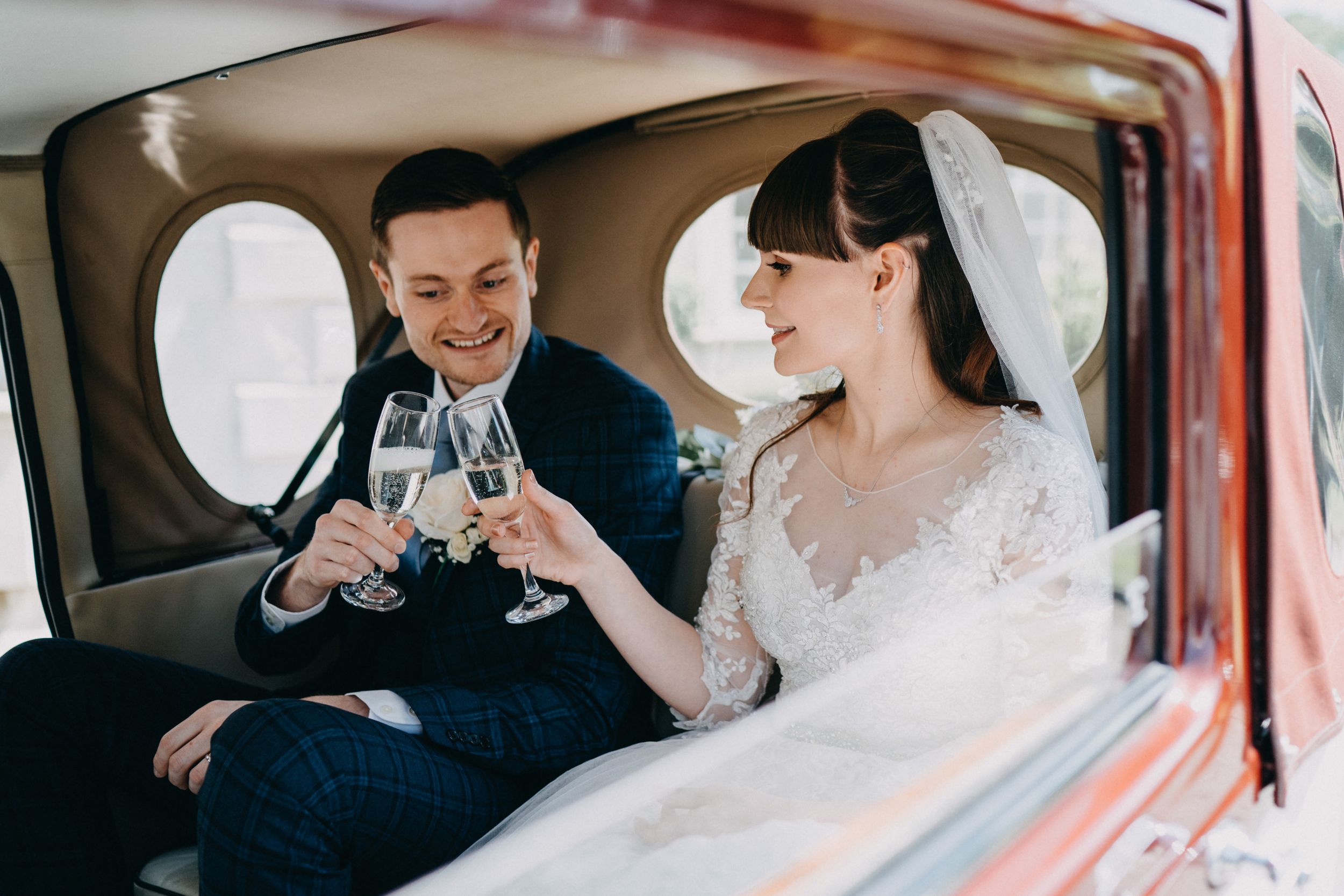 Couple toasting with champagne glasses inside vintage wedding car.