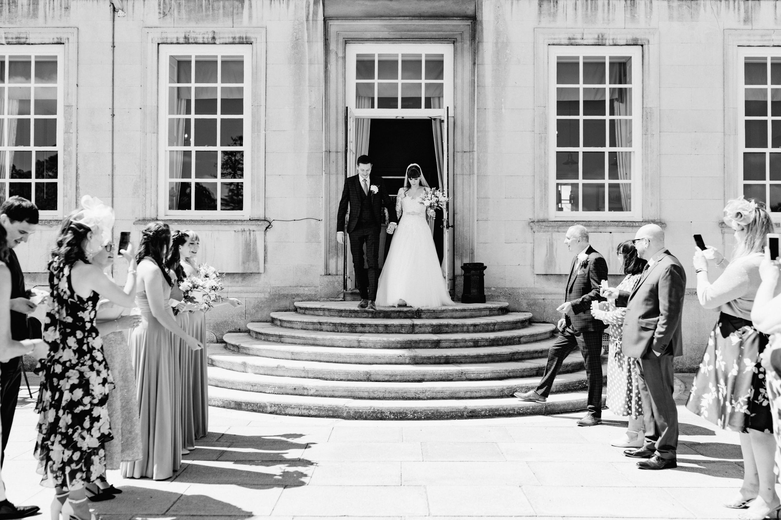 Wedding party and guests gather on grand stone steps for black and white ceremony photo.