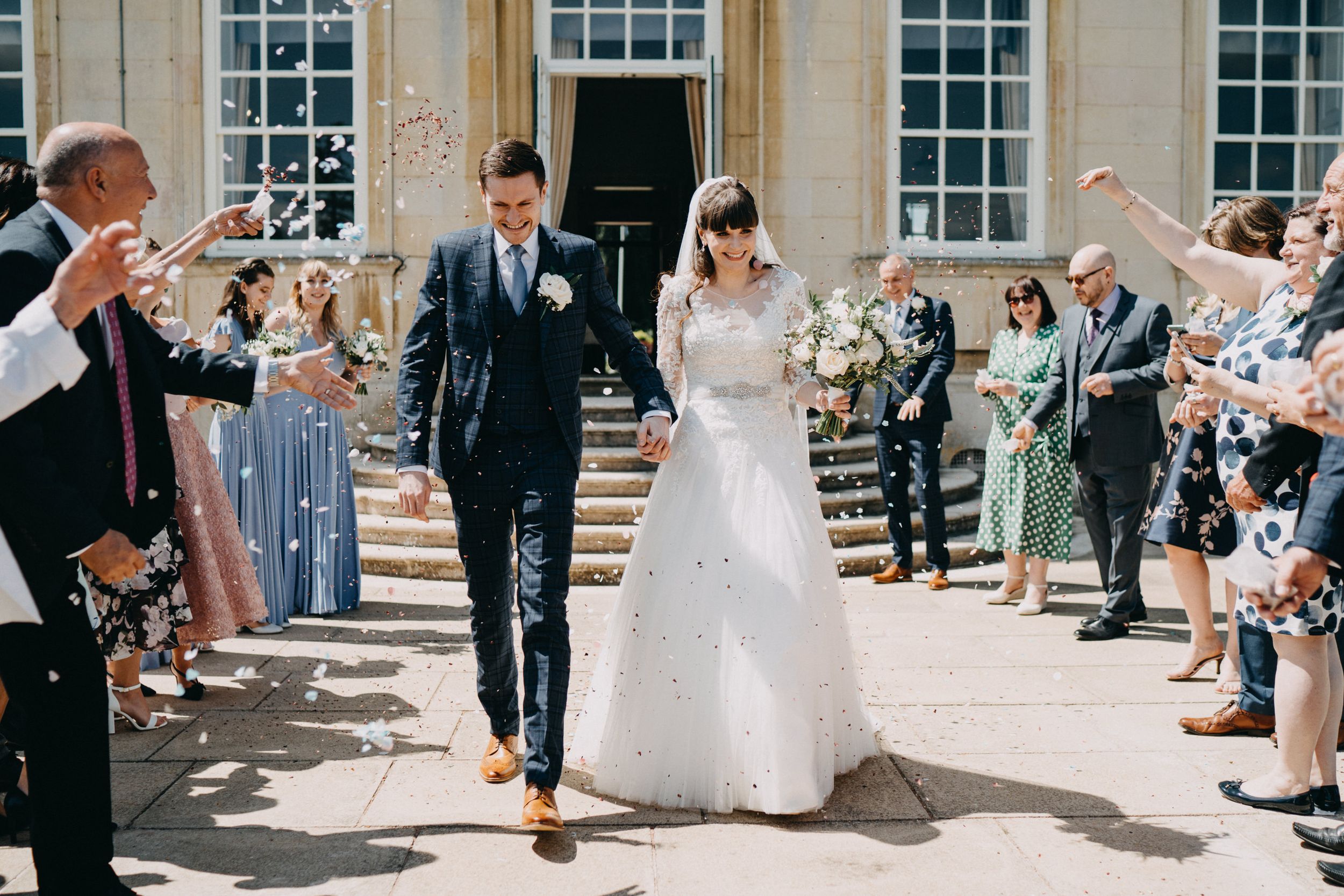 Wedding attendees throw confetti as couple exits down stone steps.