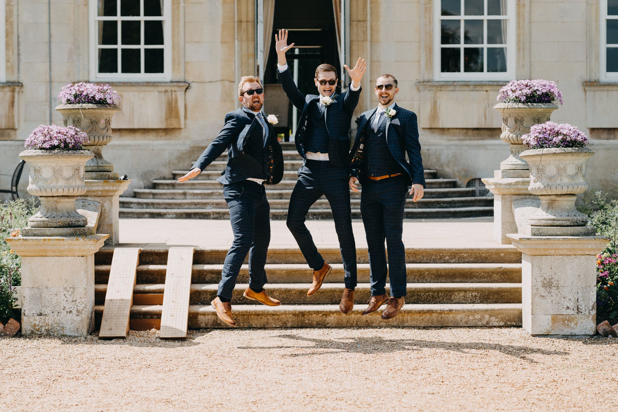 Three people jumping joyfully on stone steps with flower arrangements.