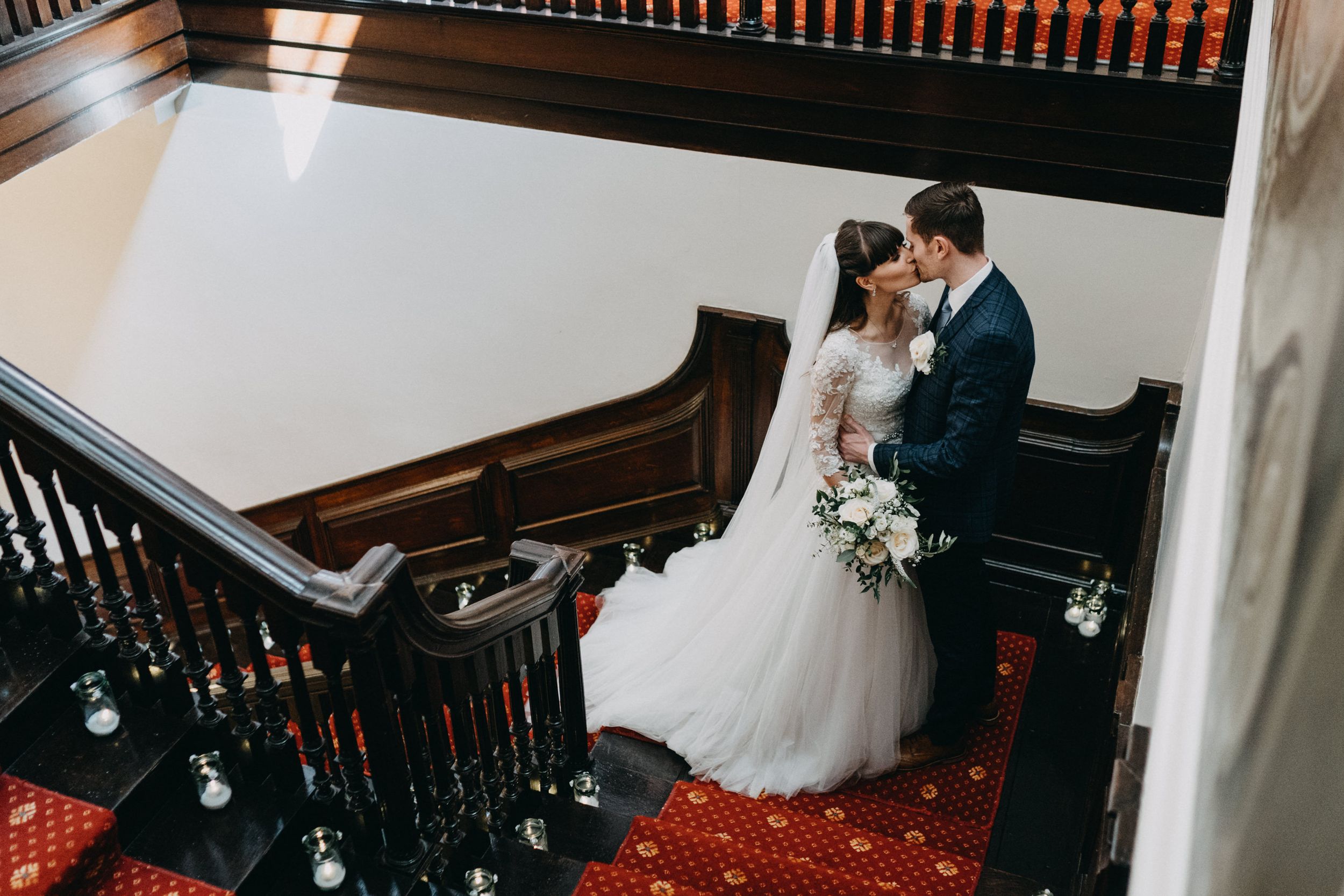 A wedding couple sharing an intimate moment on a classic staircase with red carpeting at Harrowden Hall.