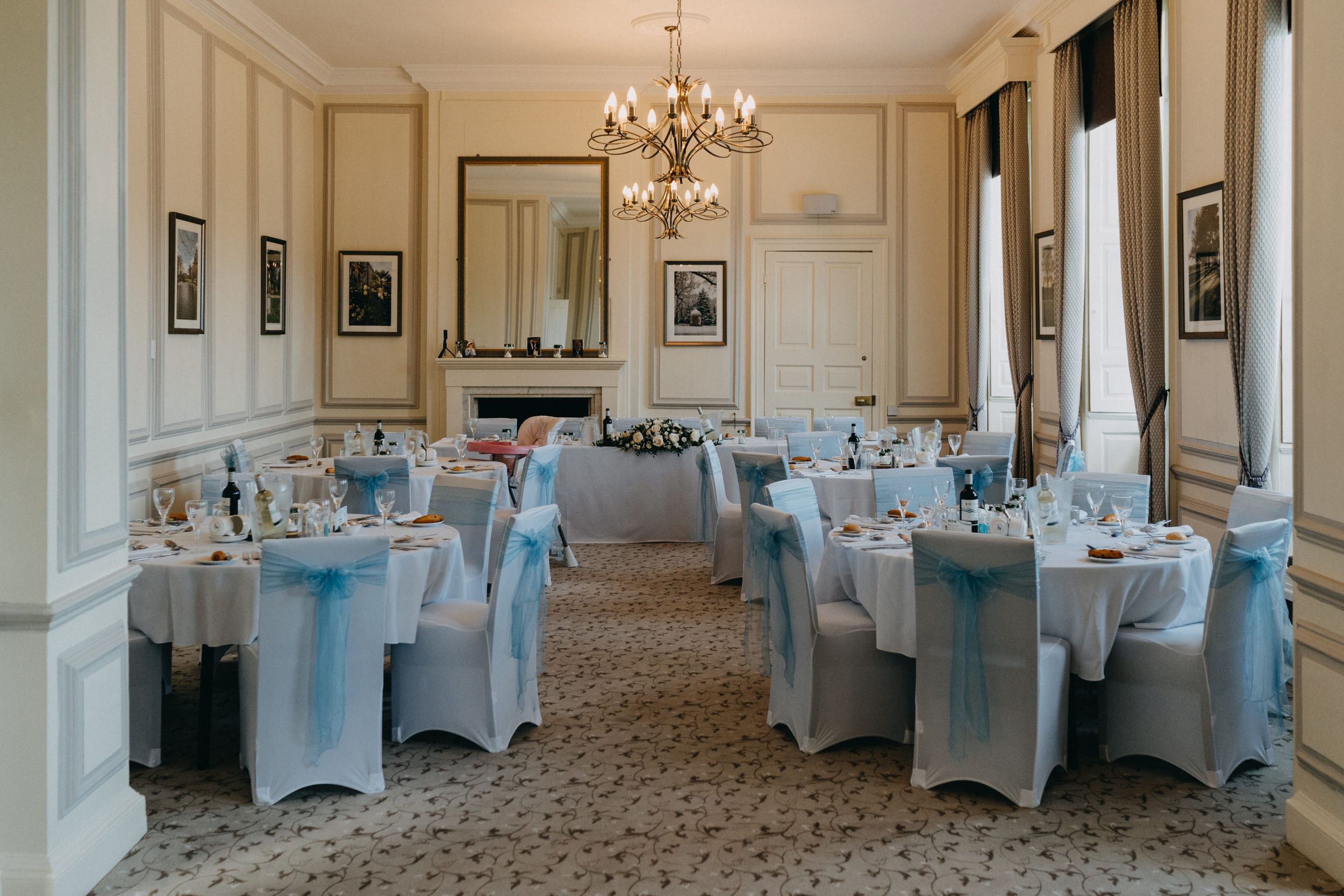 An elegant wedding reception room at Harrowden Hall with crystal chandelier and light blue chair covers.