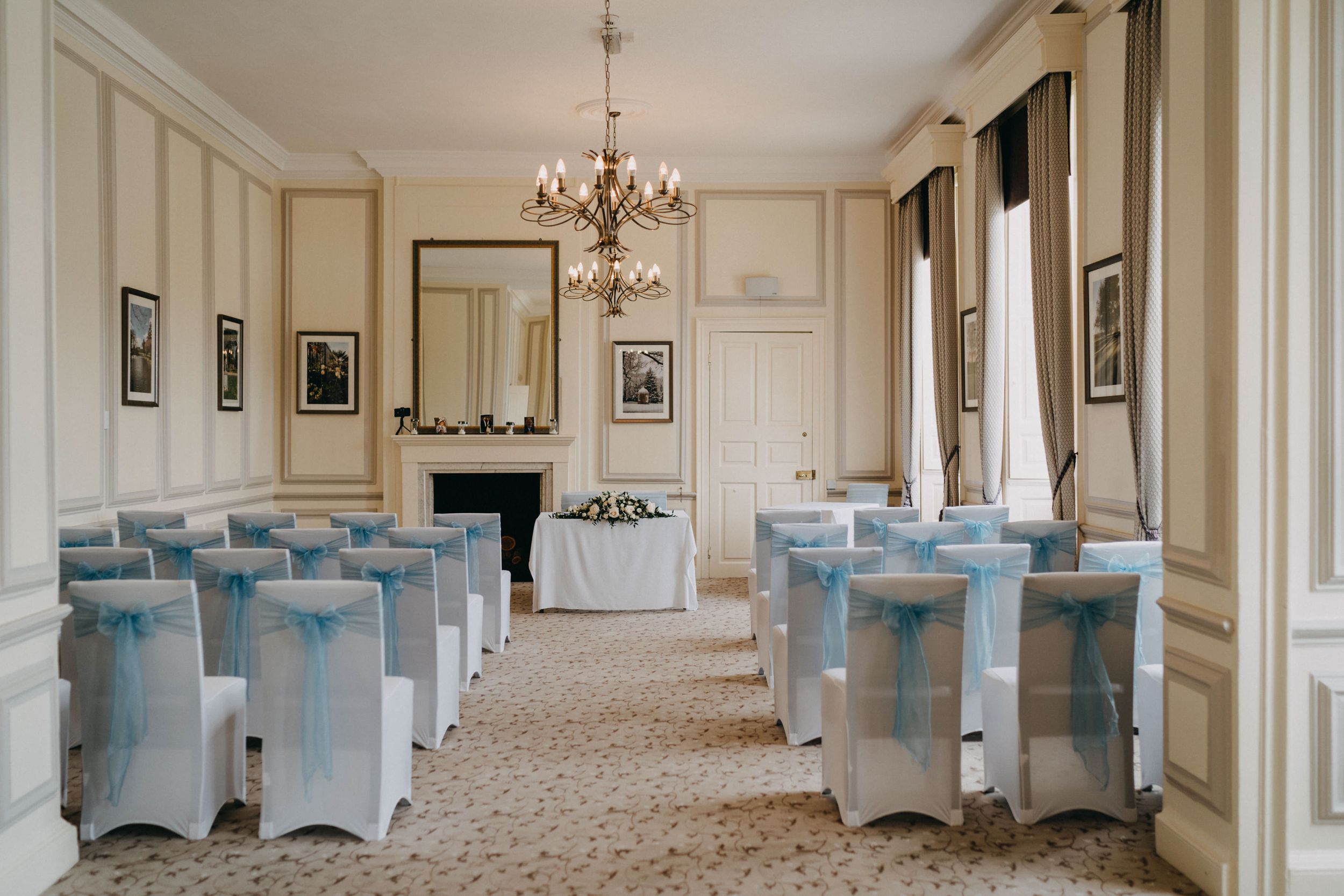 Elegant wedding ceremony room at Harrowden Hall with white chairs and blue sashes beneath a crystal chandelier.