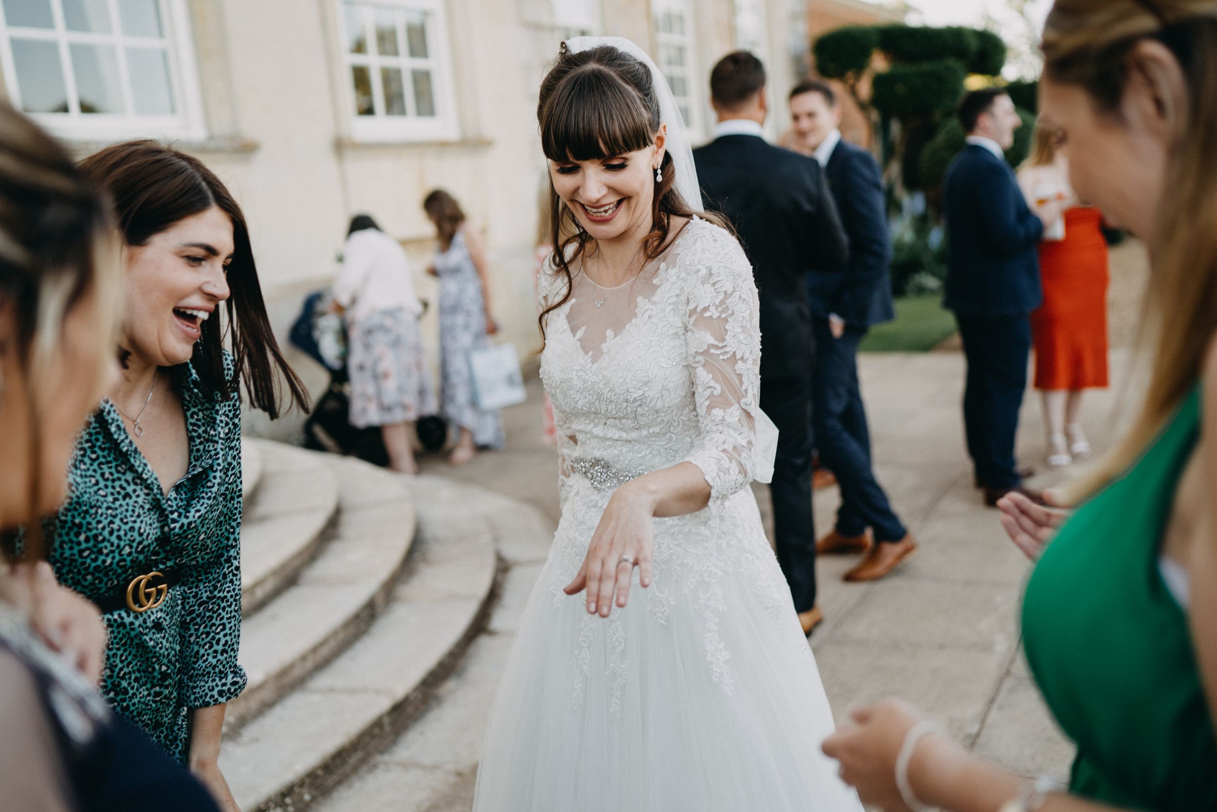 Friends admiring a beautiful lace wedding dress at an outdoor reception.