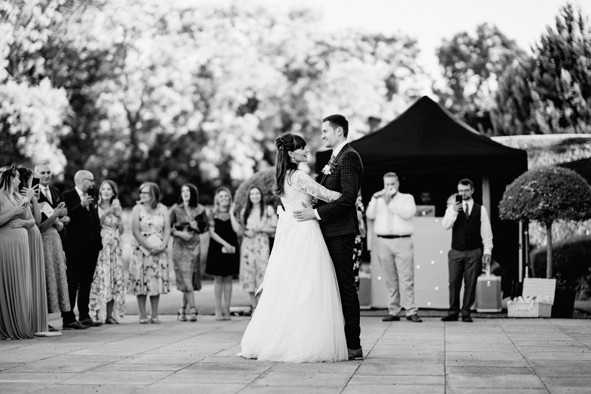 Black and white photo of couple's first dance surrounded by guests at outdoor reception, Harrowden Hall.