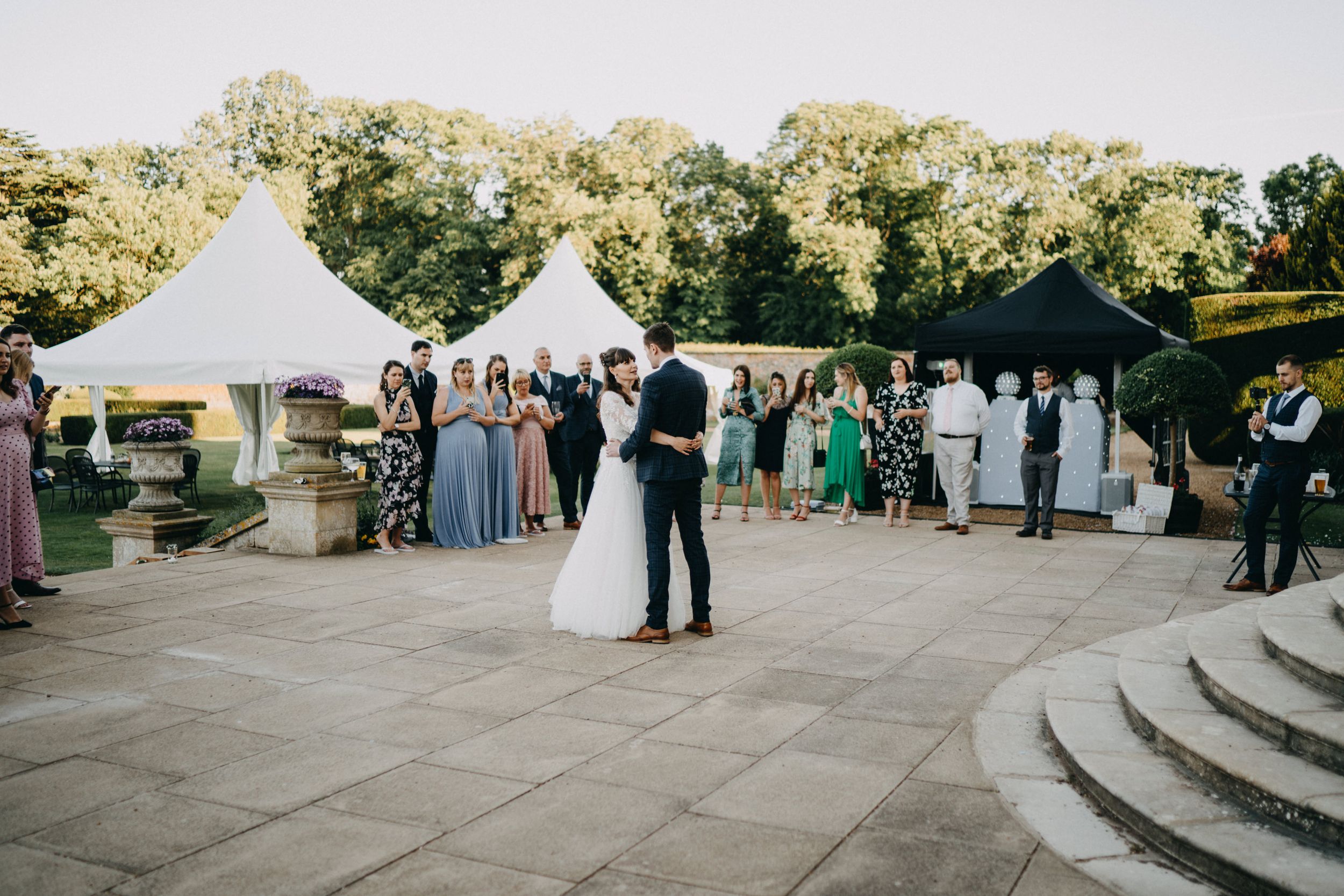 Couple sharing their first dance under outdoor tent with guests looking on.