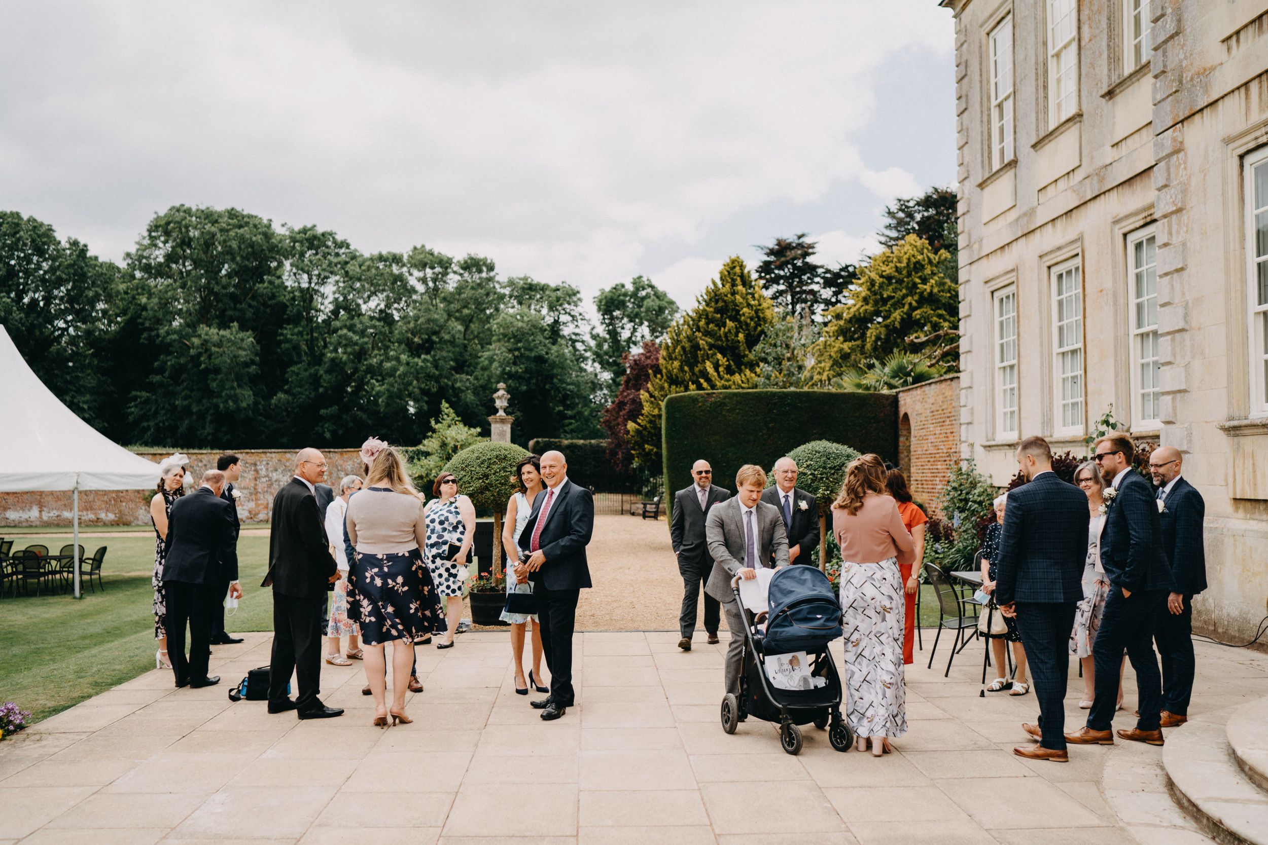 Wedding guests mingle outside a stately manor house on an overcast day at Harrowden Hall, Northamptonshire.