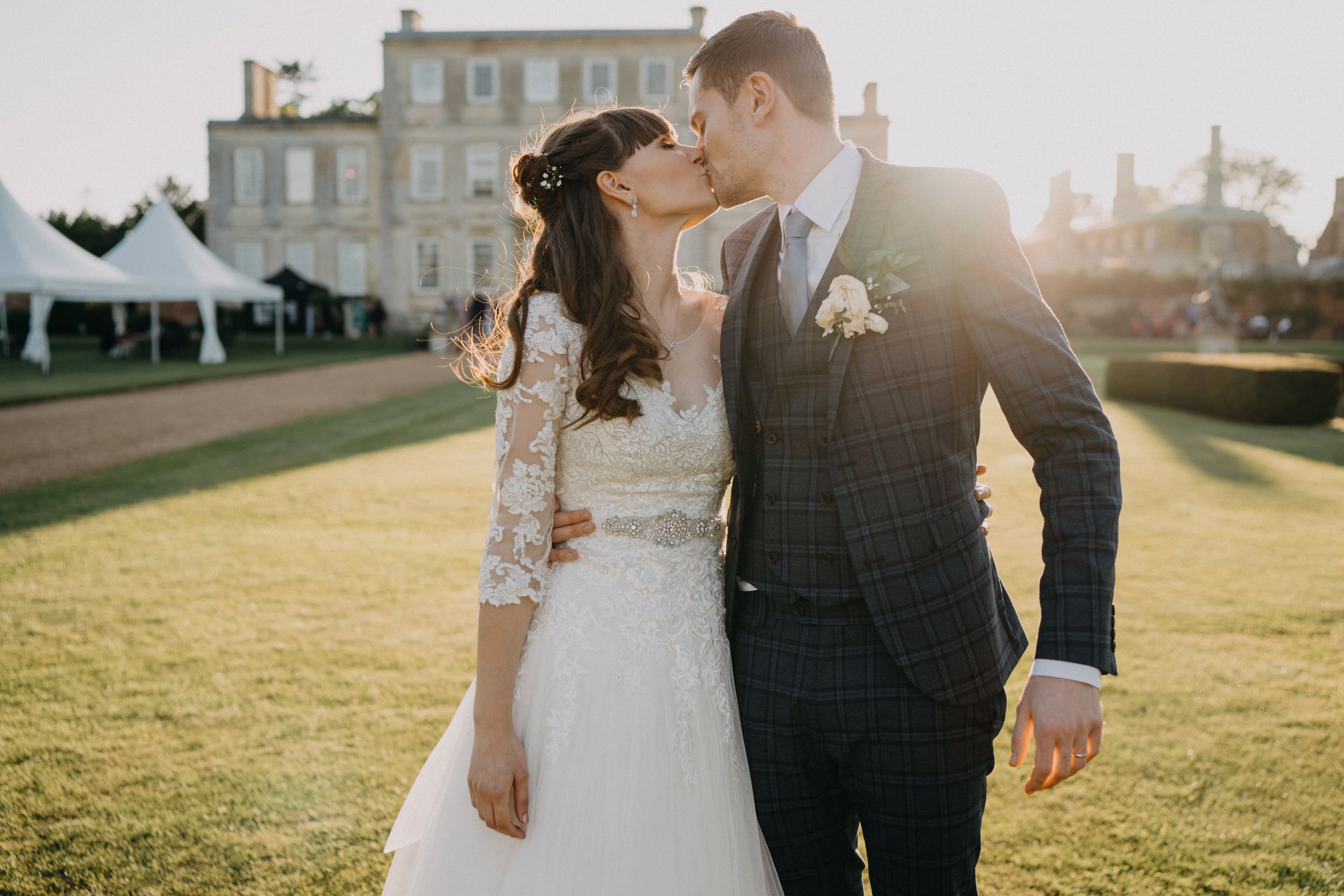 A tender wedding moment captured in golden sunlight with Harrowden Hall in the background.