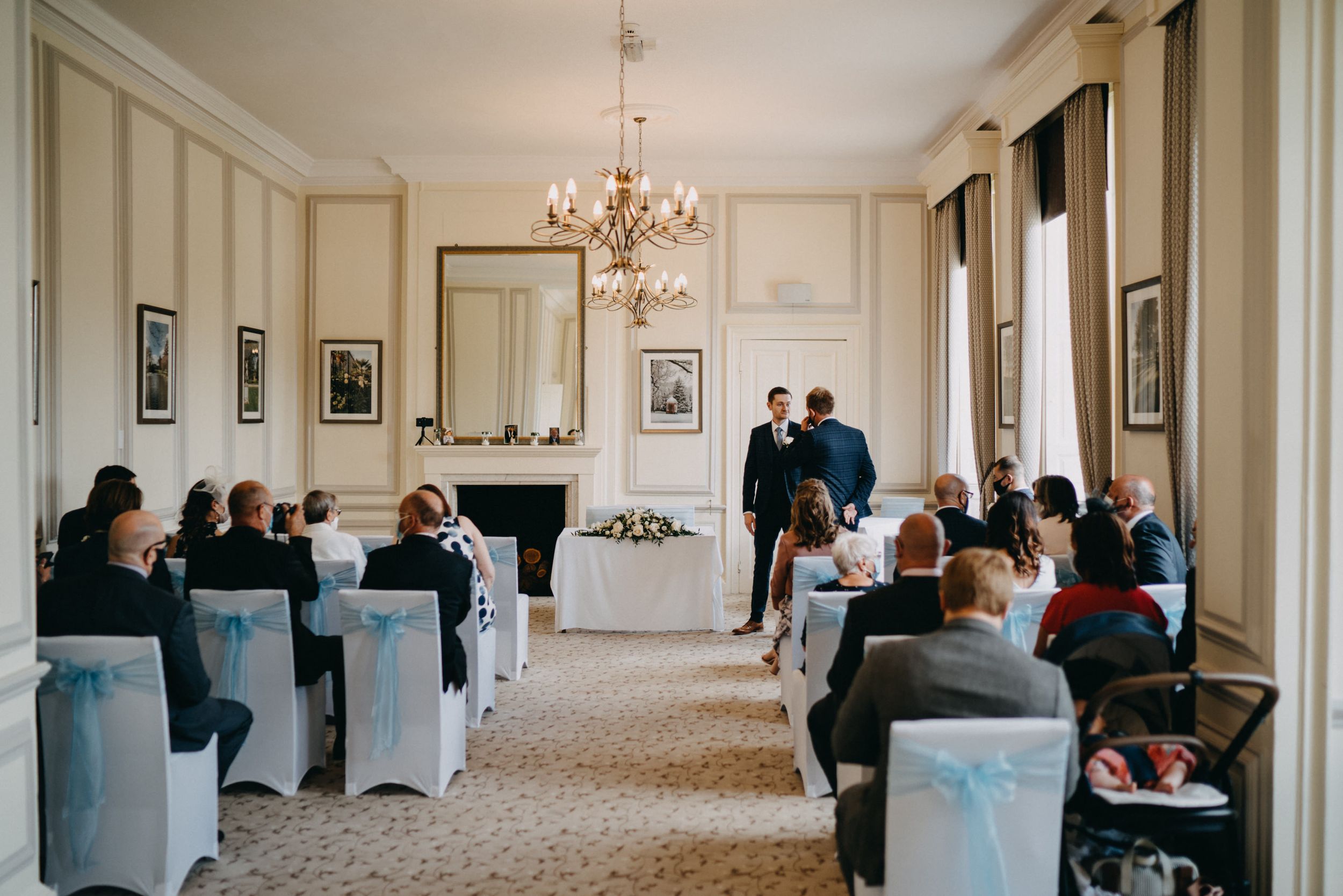 Wedding ceremony in progress in an elegant room at Harrowden Hall with blue-accented chairs.