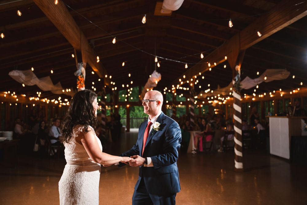 A couple shares their first dance in a rustic barn venue decorated with twinkling string lights overhead.