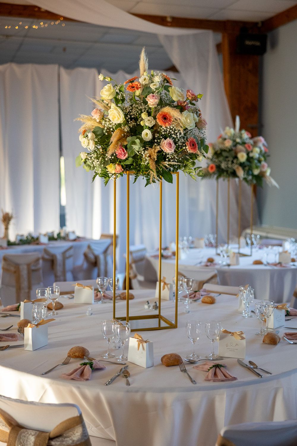 Elegant wedding centerpiece with tall gold stands and lush floral arrangements on a white tablecloth.